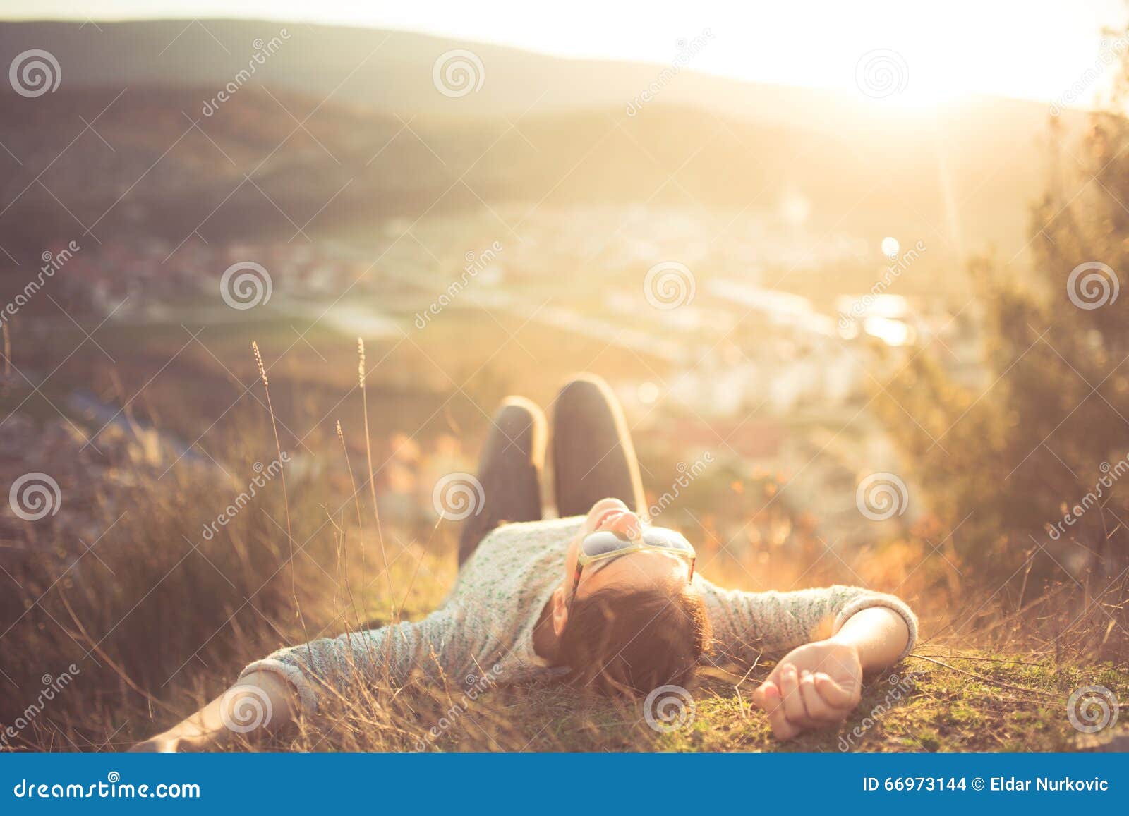 carefree happy woman lying on green grass meadow on top of mountain edge cliff enjoying sun on her face. enjoying nature sunset