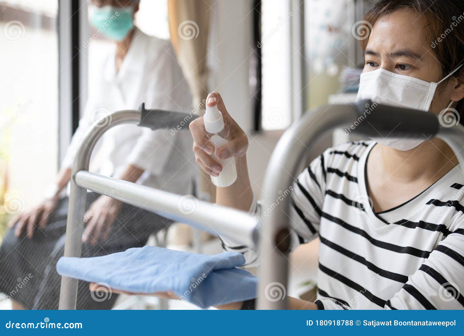 caregiver in a mask,using spraying alcohol antiseptic,disinfecting spray,cleaning on walking aids,walker for the senior,during