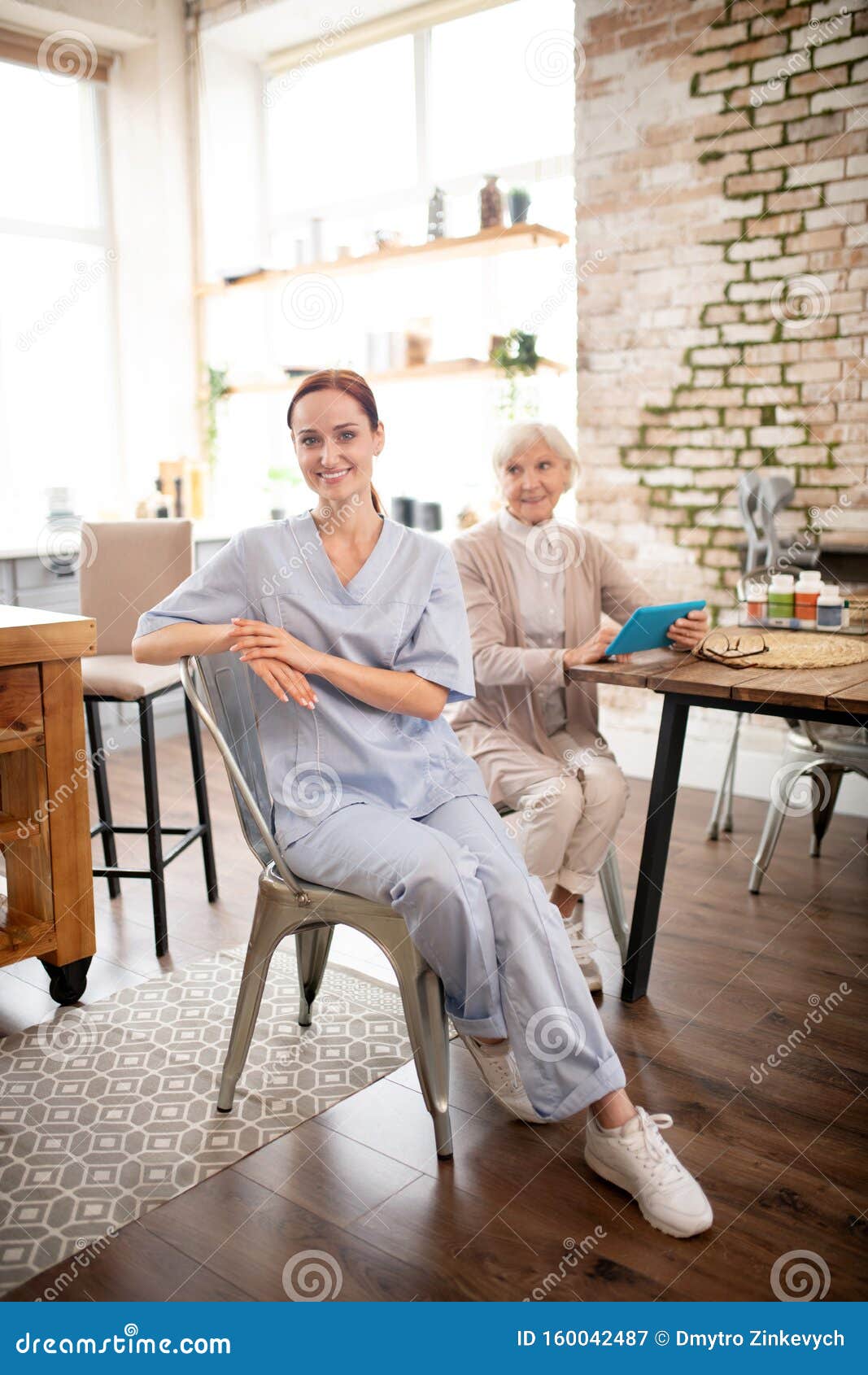 Caregiver Wearing Uniform And Sneakers Visiting Pensioner Stock Image Image Of Redhaired