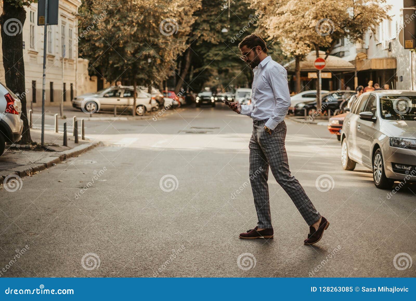 Man on mobile phone cross the road at a pedestrian crossing. Ho