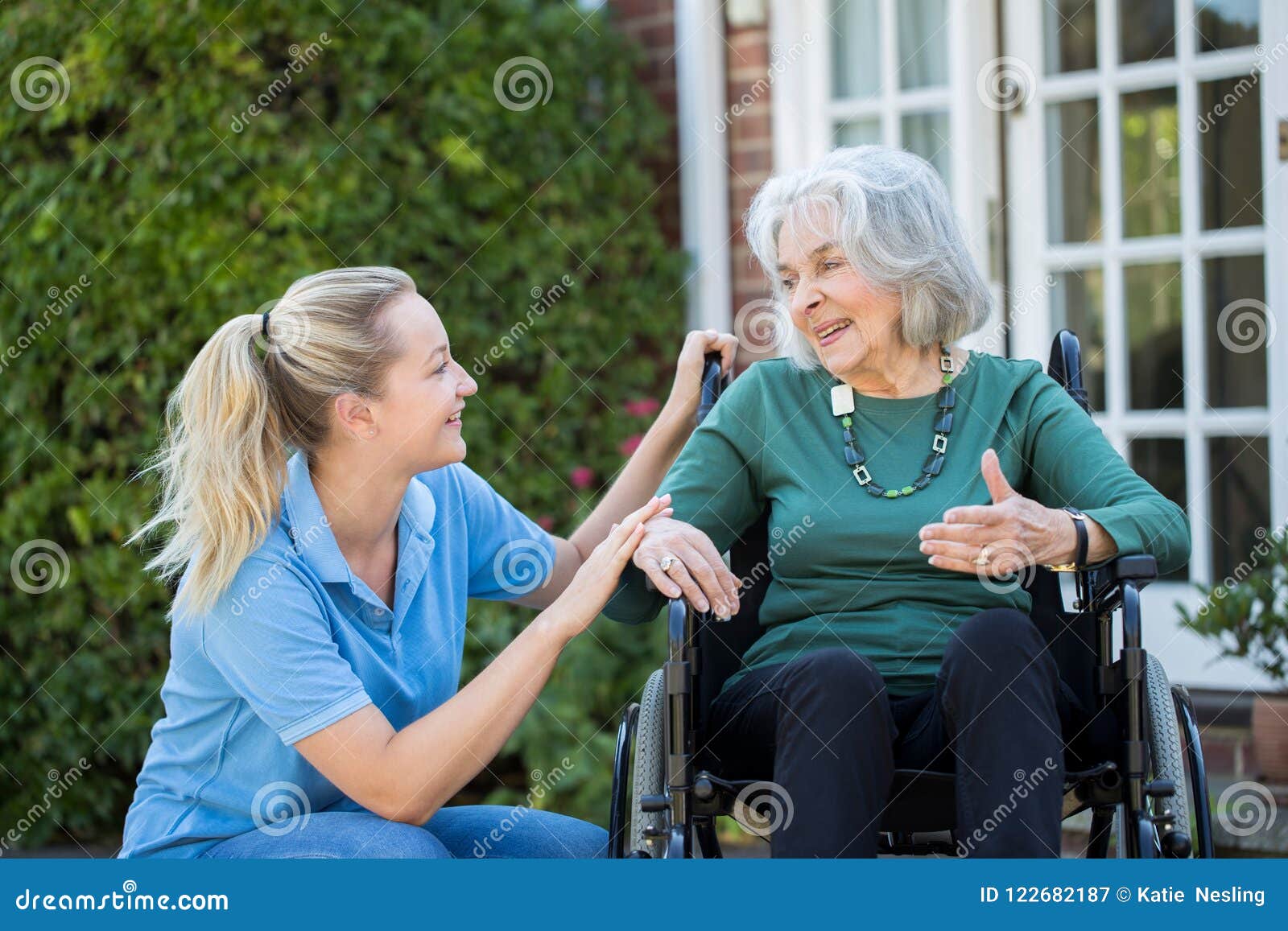 carer pushing senior woman in wheelchair outside home