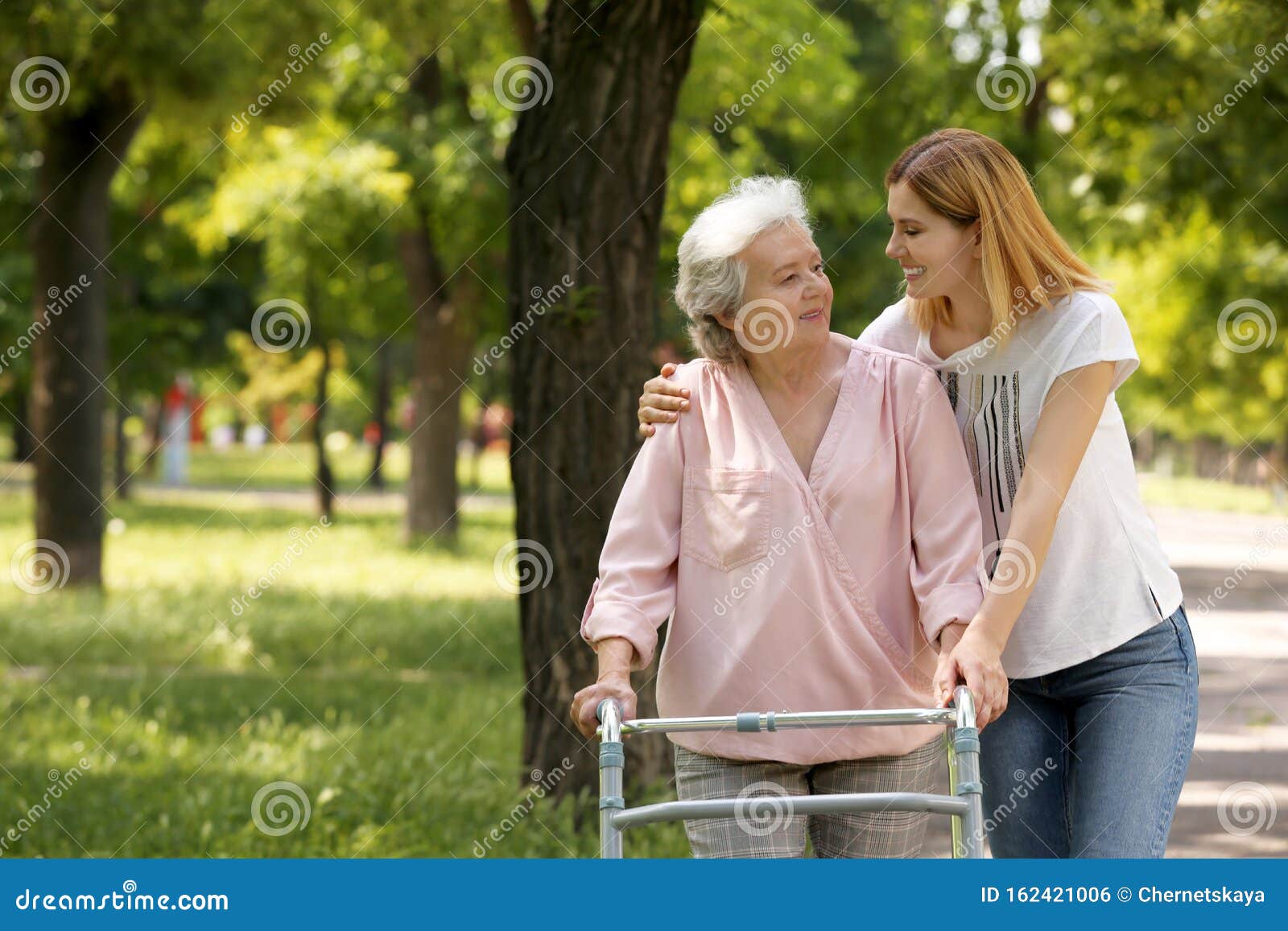 caretaker helping elderly woman with walking frame