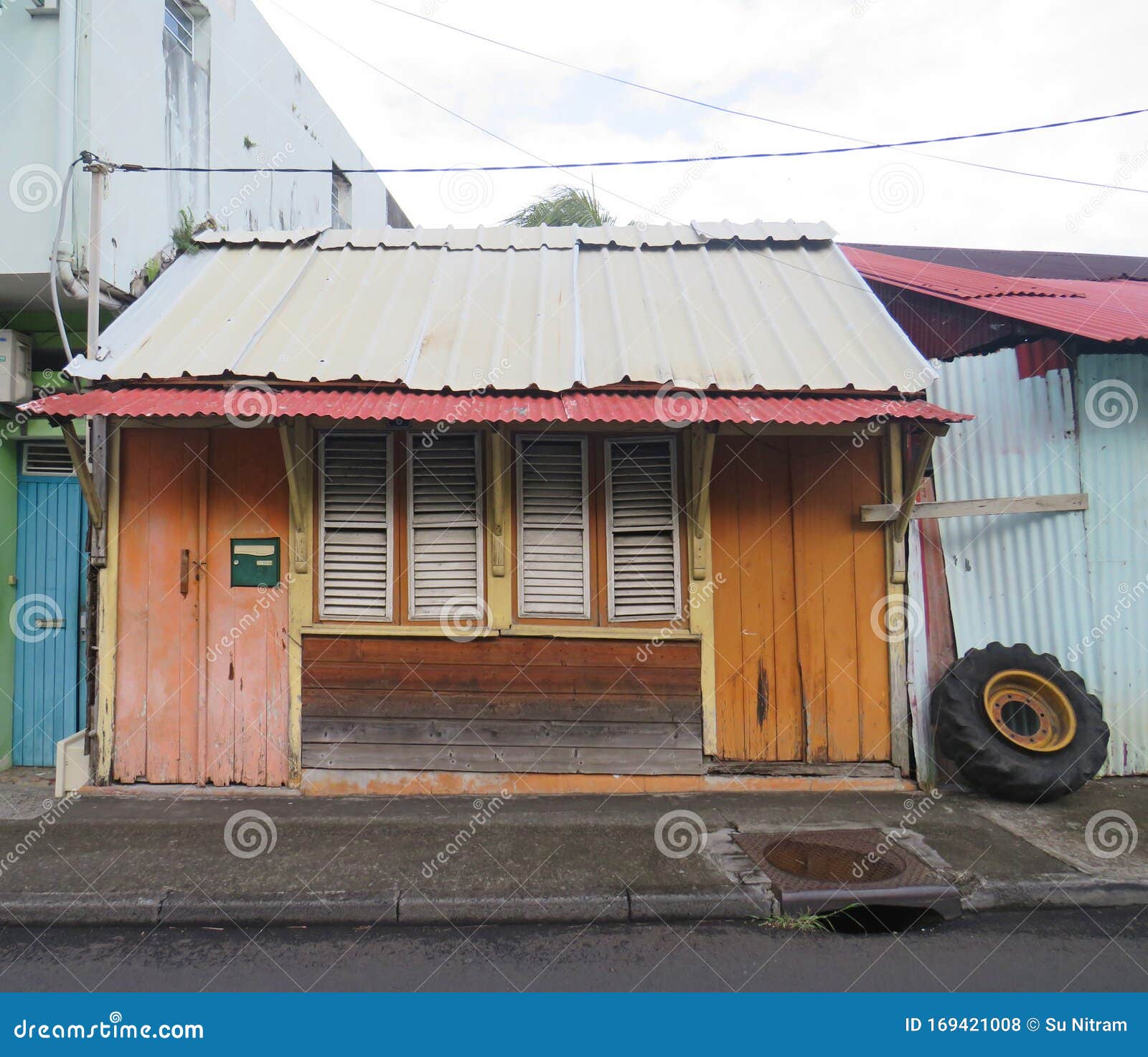 caribbean wooden house with orange doors, tin roof and closed white window shutters. caribbean architecture