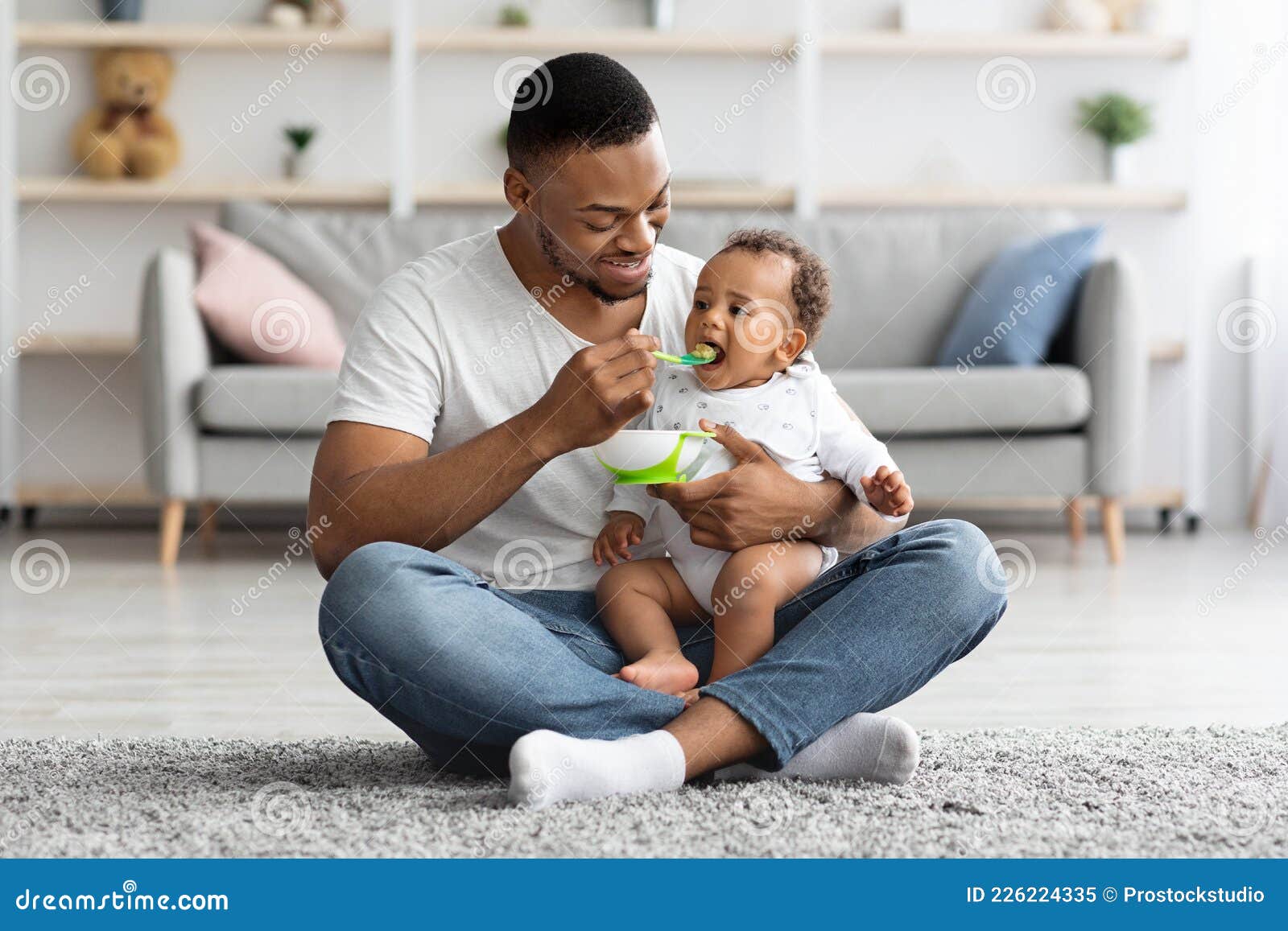 caring black dad feeding his adorable infant baby from spoon at home