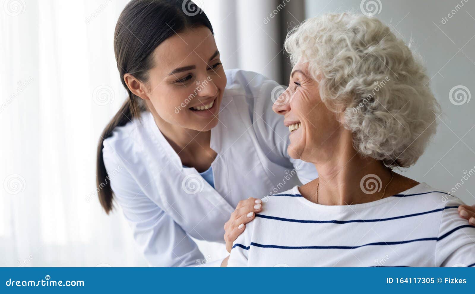 caring smiling young nurse taking care of elder grandma patient