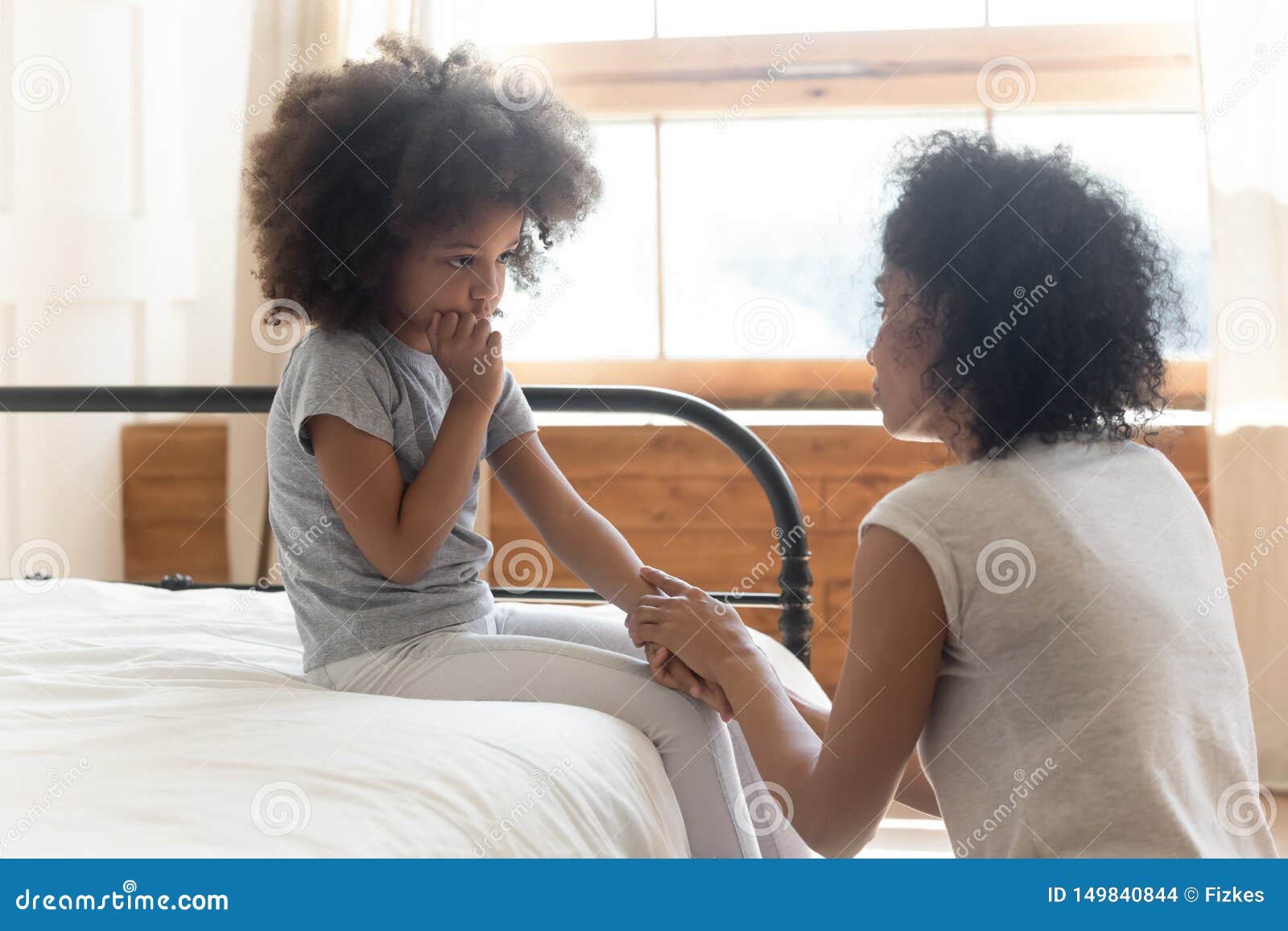 worried african mother holding hand comforting sad little daughter