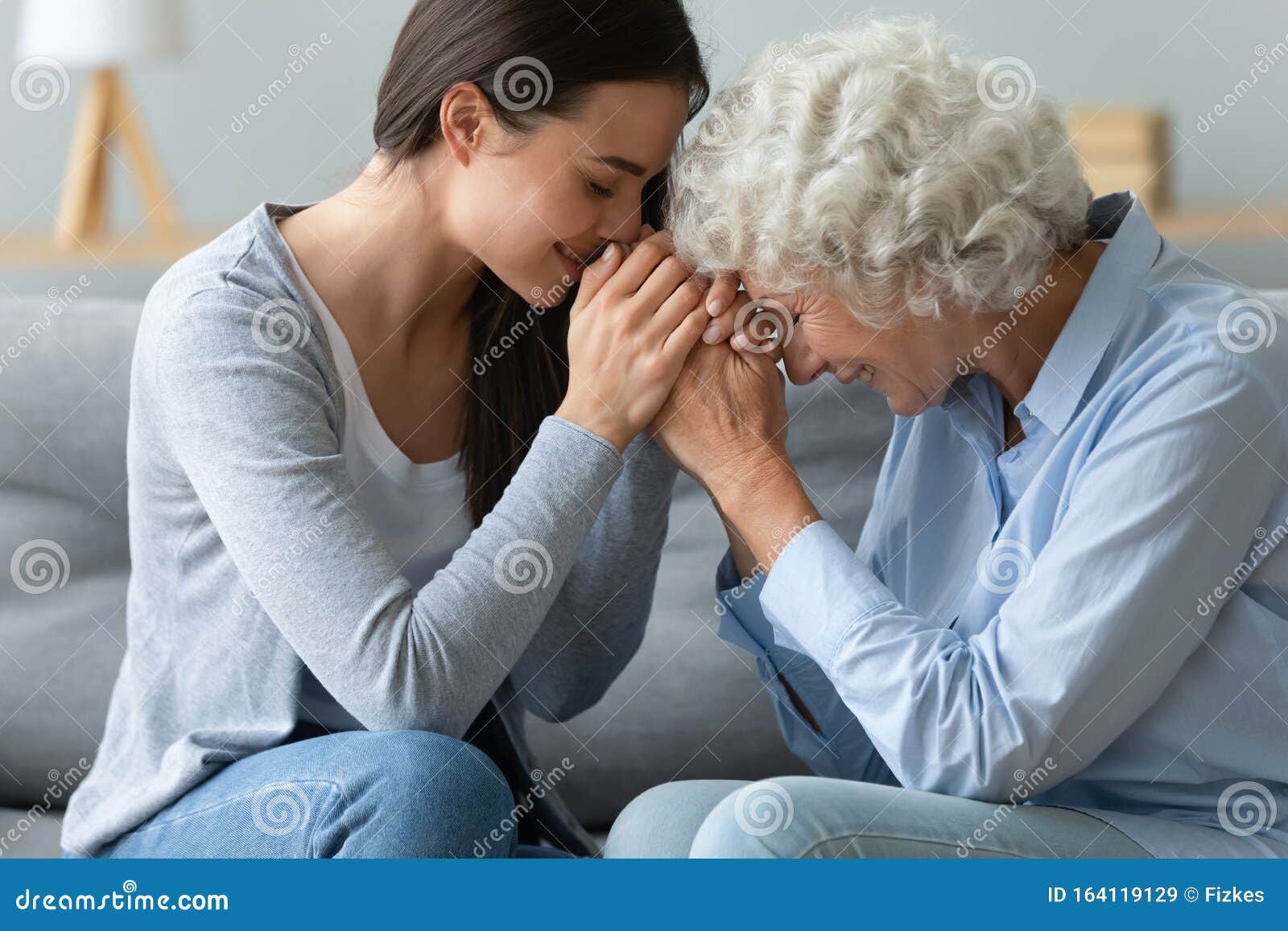 caring young adult woman granddaughter hold hands of old grandmother