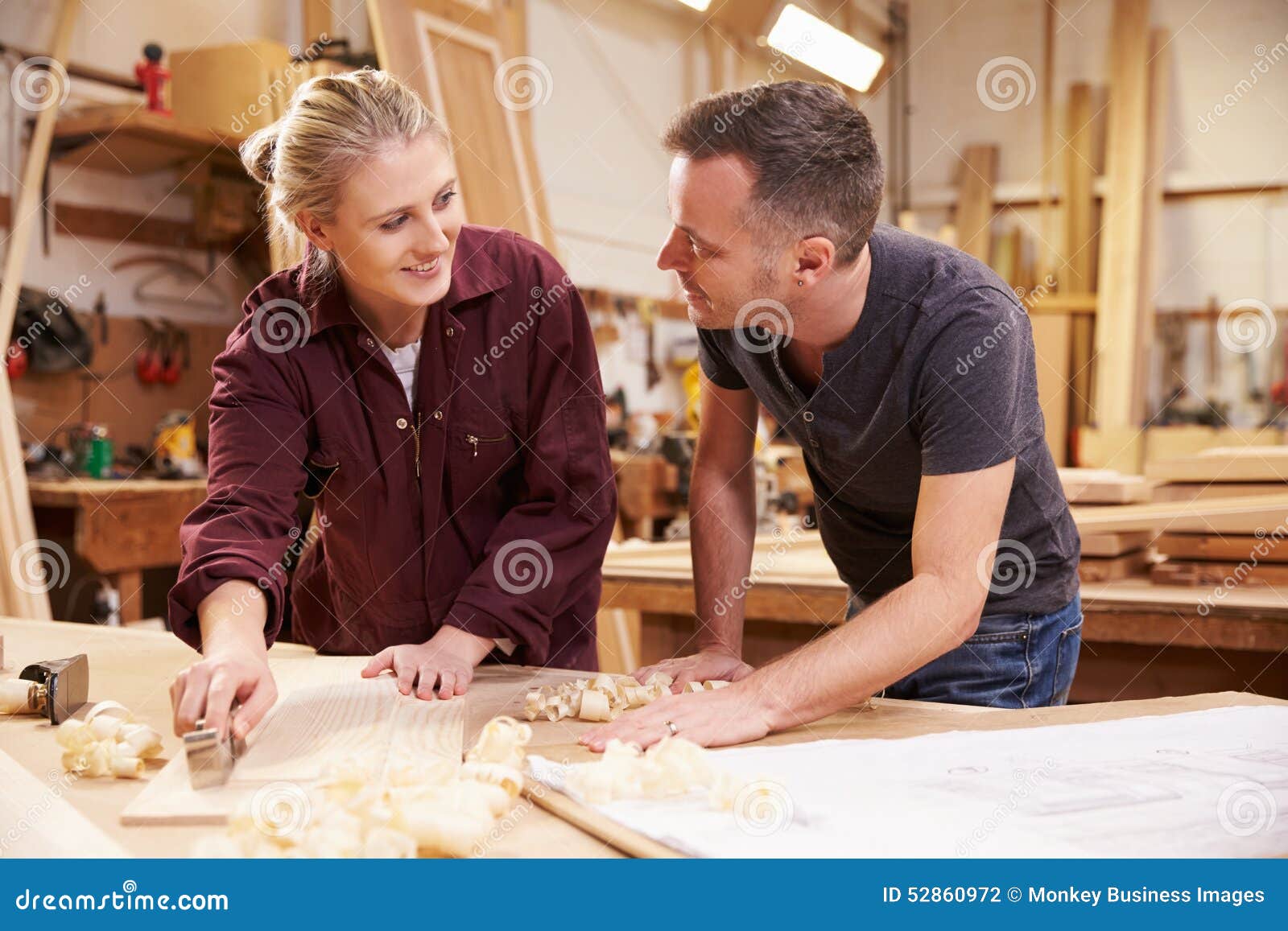 Carpenter with Female Apprentice Planing Wood in Stock Photo