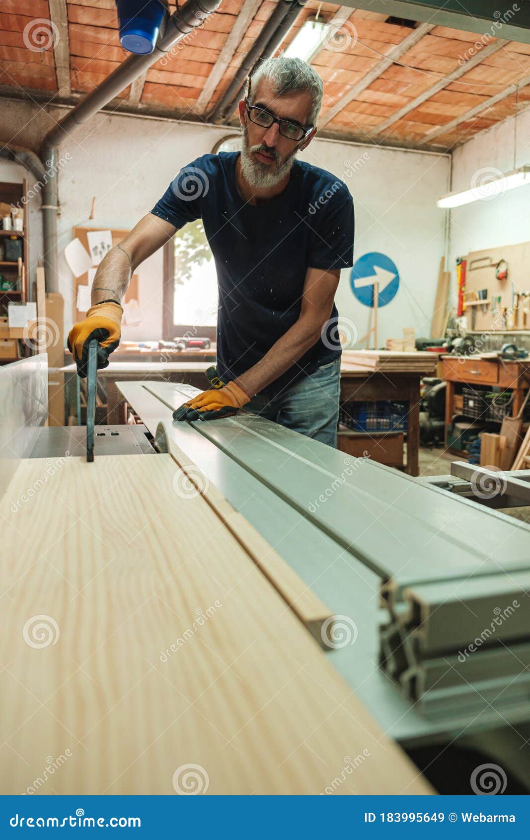 Carpenter Pushing a Piece of Wood into the Saw Cutting Machine Stock