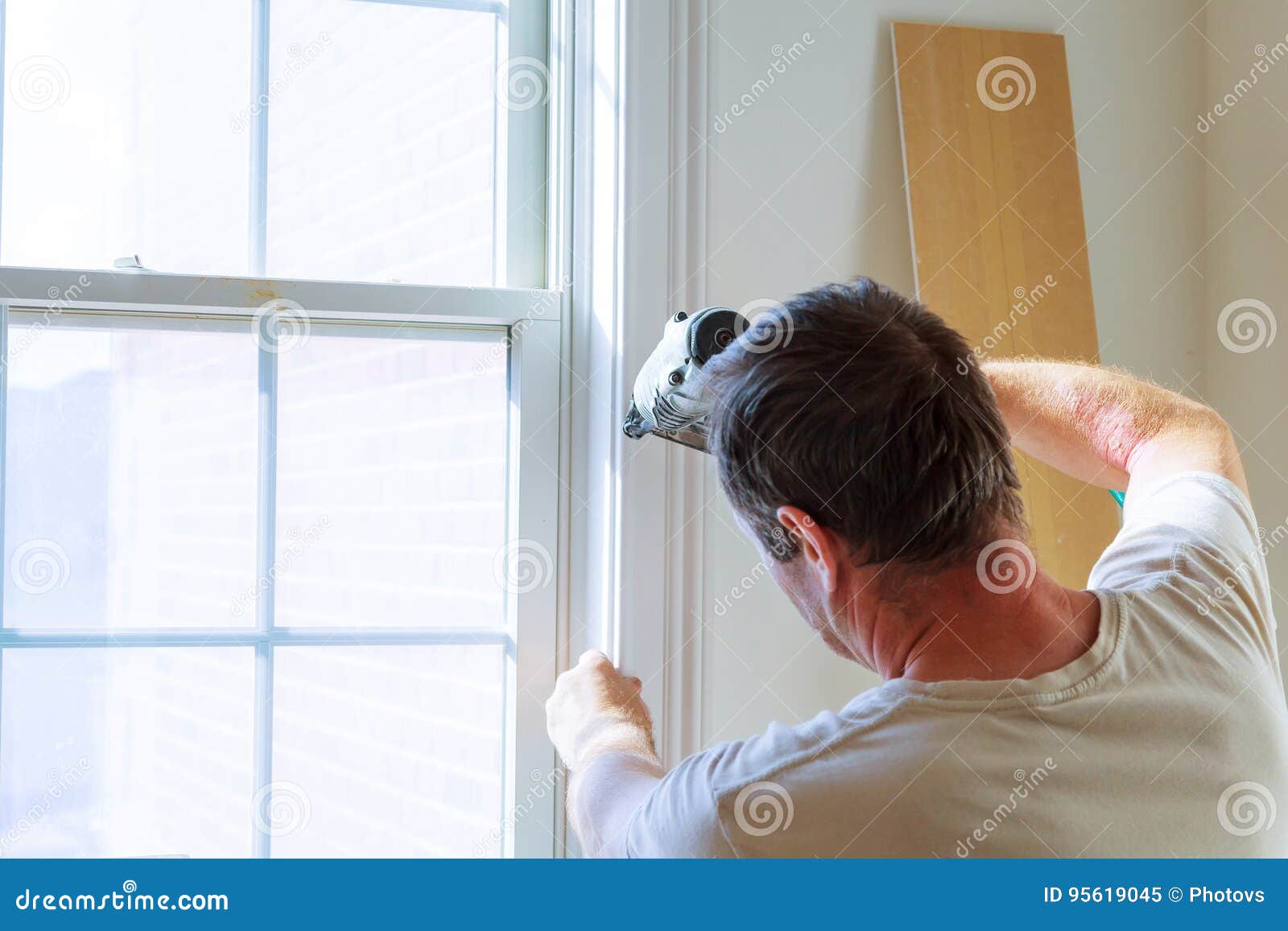 carpenter using nail gun to moldings on windows, framing trim,