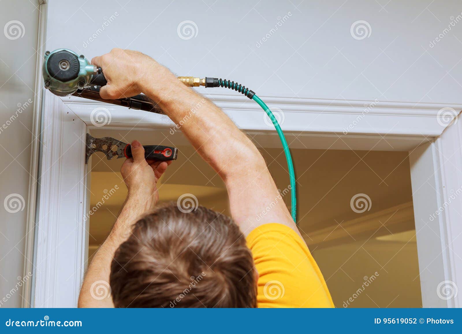 carpenter using nail gun to moldings on windows, framing trim,