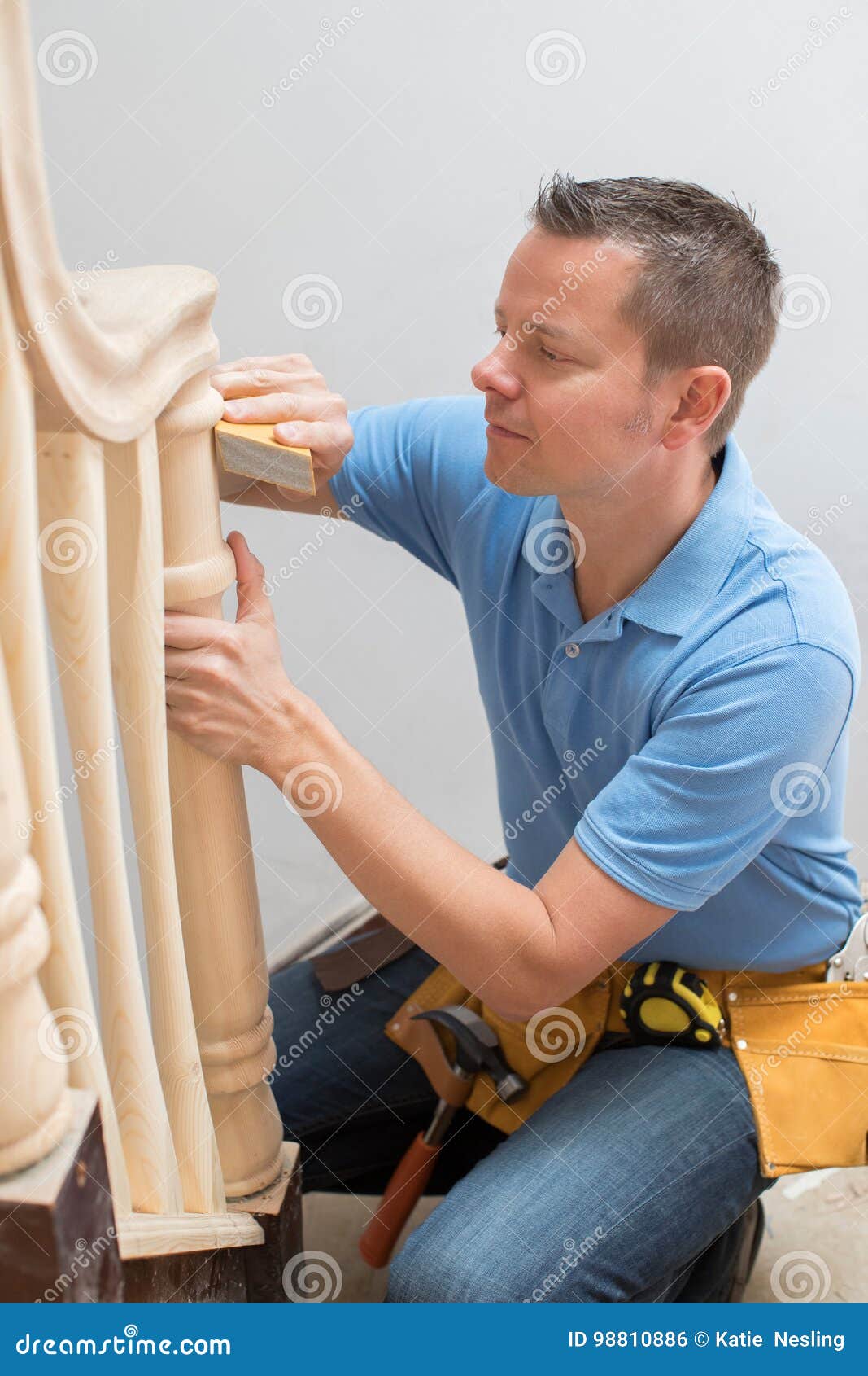 carpenter using sandpaper on bannister in home