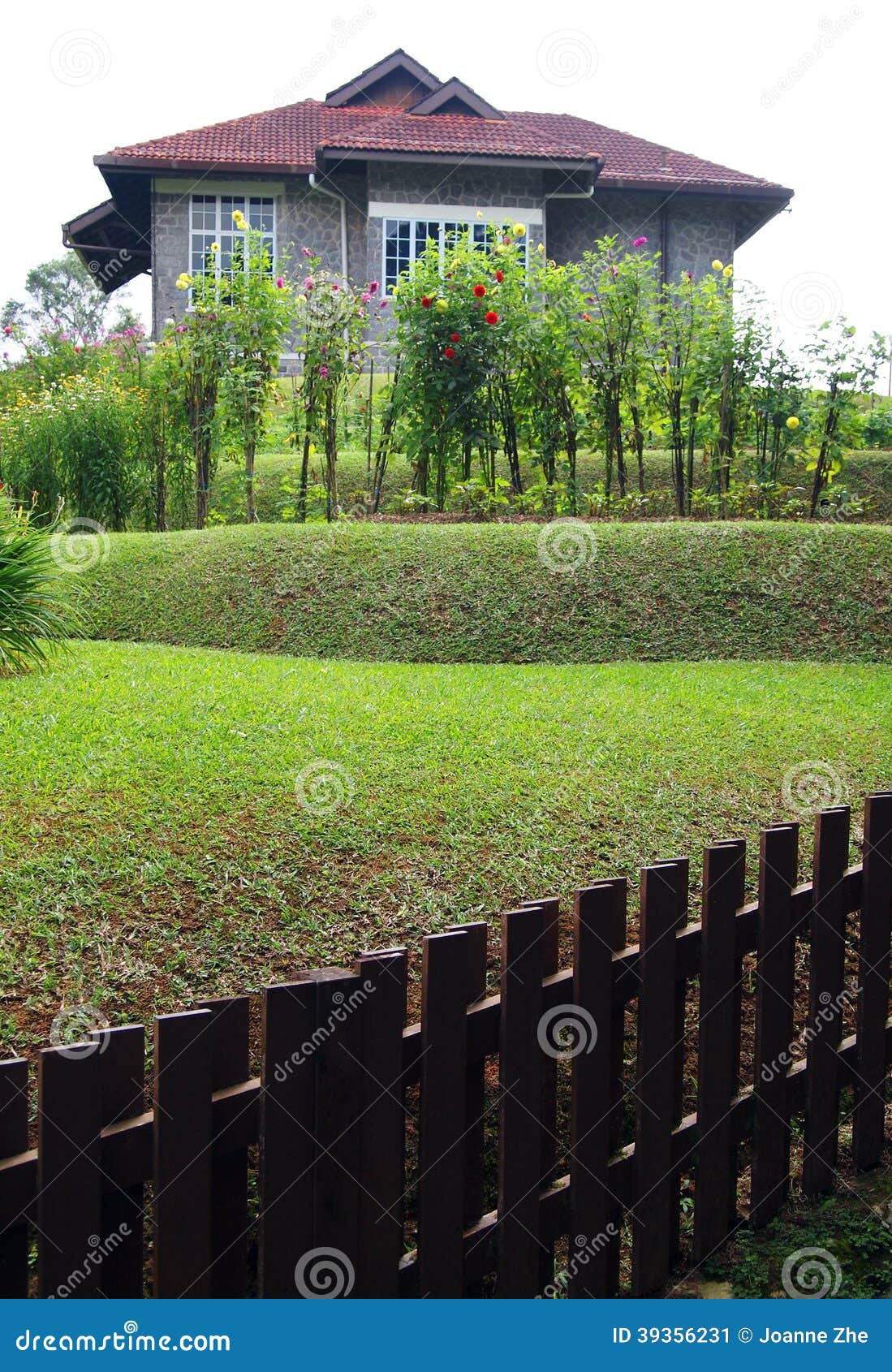 Casa de pedra velha com jardim e a cerca terraced. Uma fotografia que mostra a um estilo antigo a casa de pedra cinzenta velha no estilo colonial britânico, com jardim do terraço no montanhês e em uma cerca de madeira marrom do jardim.  Imagem do conceito para o projeto do jardim ao longo de um lado inclinado do monte.   O lugar está no recurso das montanhas do monte de Fraser, Pahang, Malásia, 3Sudeste Asiático.