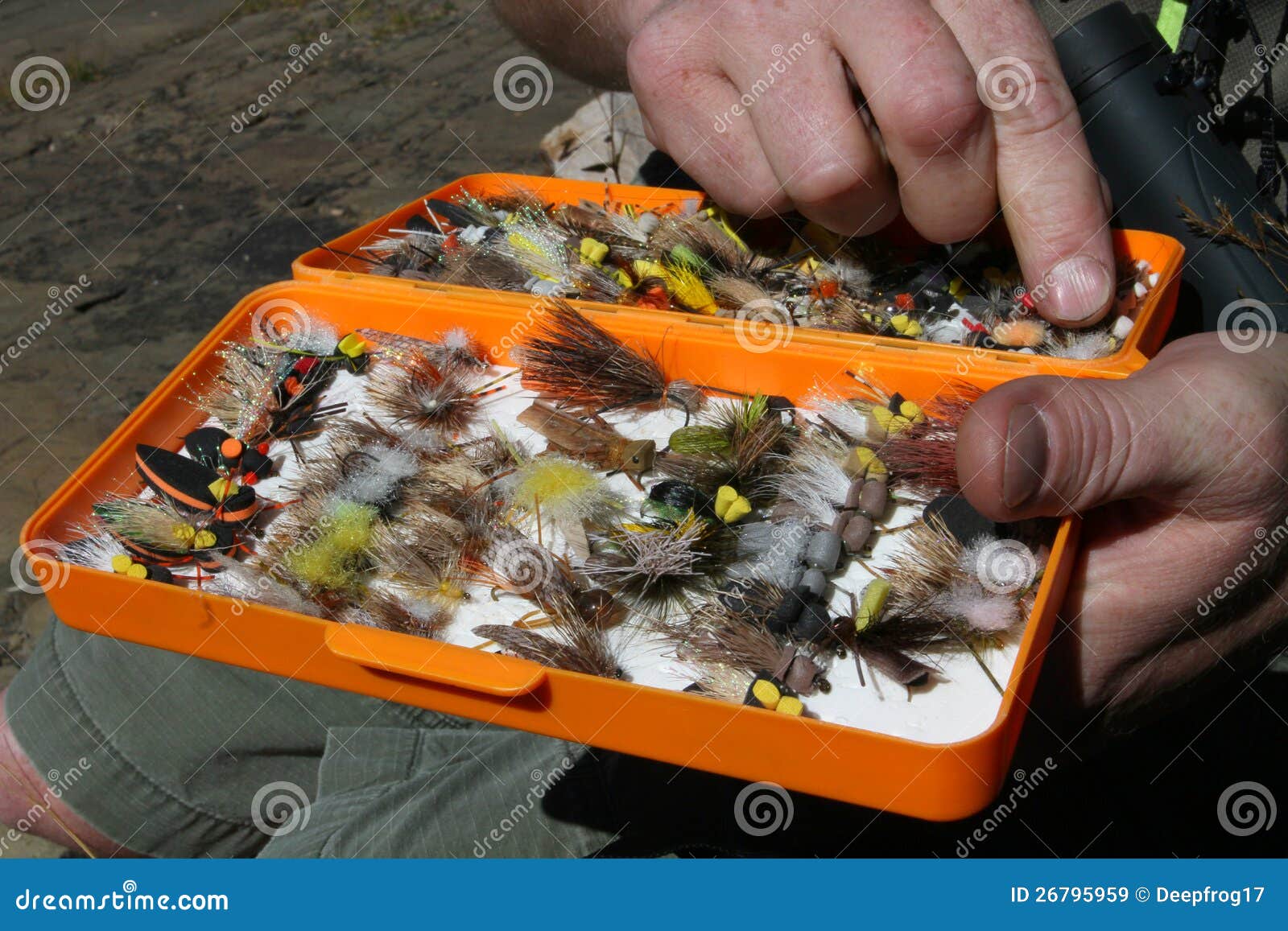 Uomo che sceglie una mosca o un richiamo mano-legata dalla sua casella di attrezzatura di pesca della mosca.