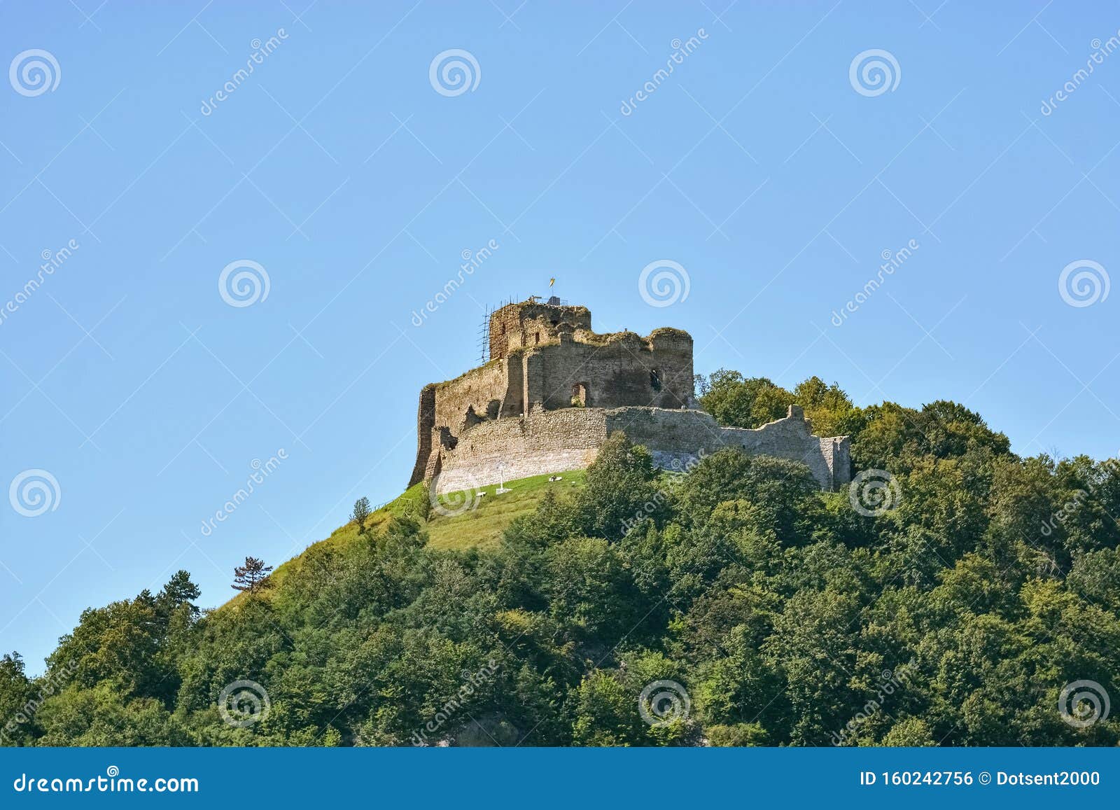 Castle on the mountain. Kapusan castle ruins, on top of a forested mountain, with a flag on a tower against a clear blue sky in Slovakia, near the town of Presov