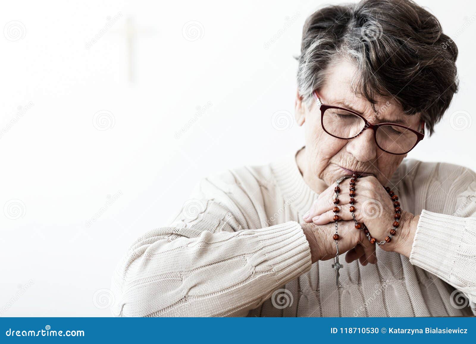 catholic grandmother in melancholy praying to god with red rosary with cross