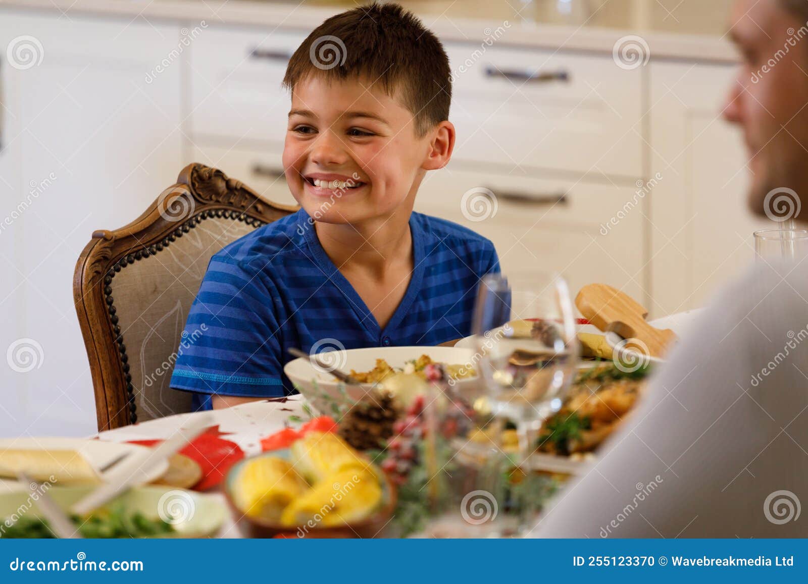 Caucasian Boy Sitting at Table during Dinner with Family and Smiling