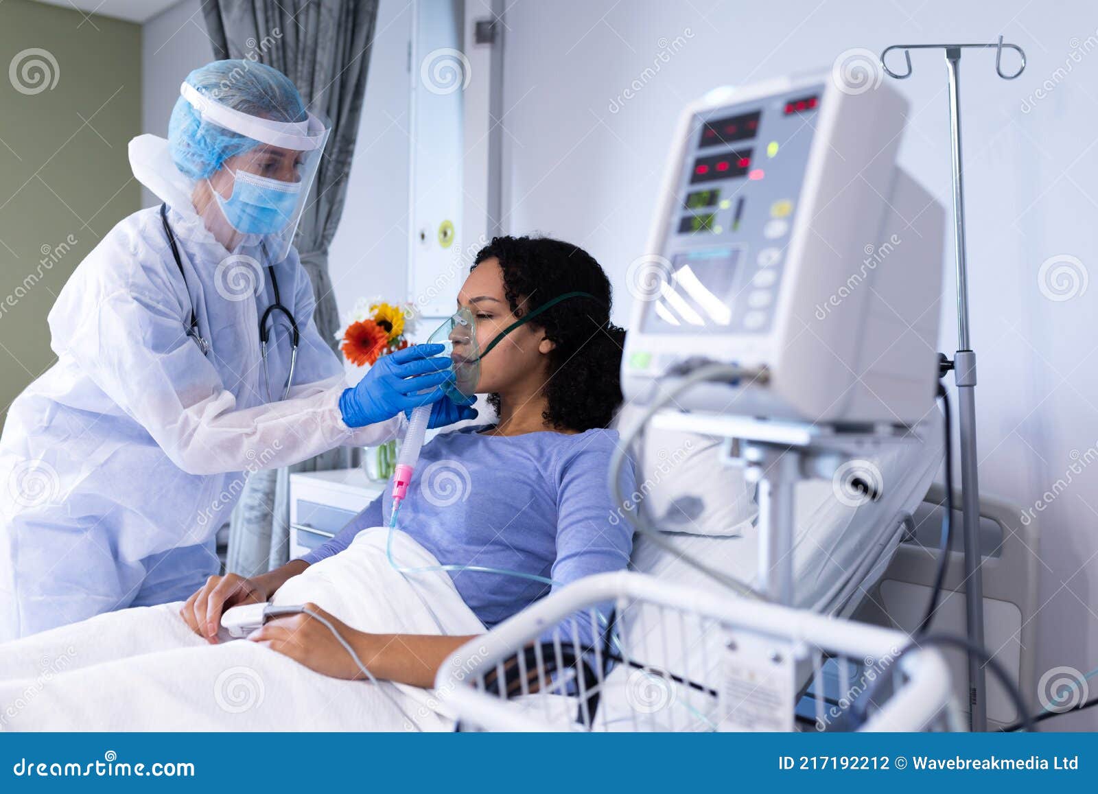 caucasian female doctor in ppe suit checking african american female patient with ventilator