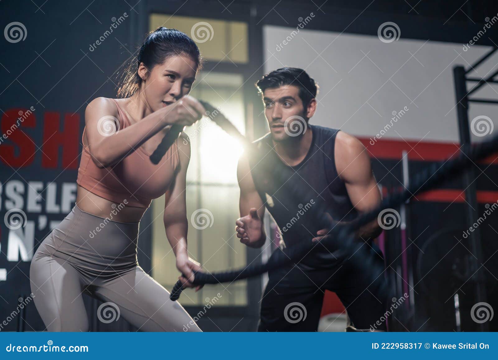 caucasian fitness trainer or instructor instruct and motivate young active beautiful sport girl using battle rope making double