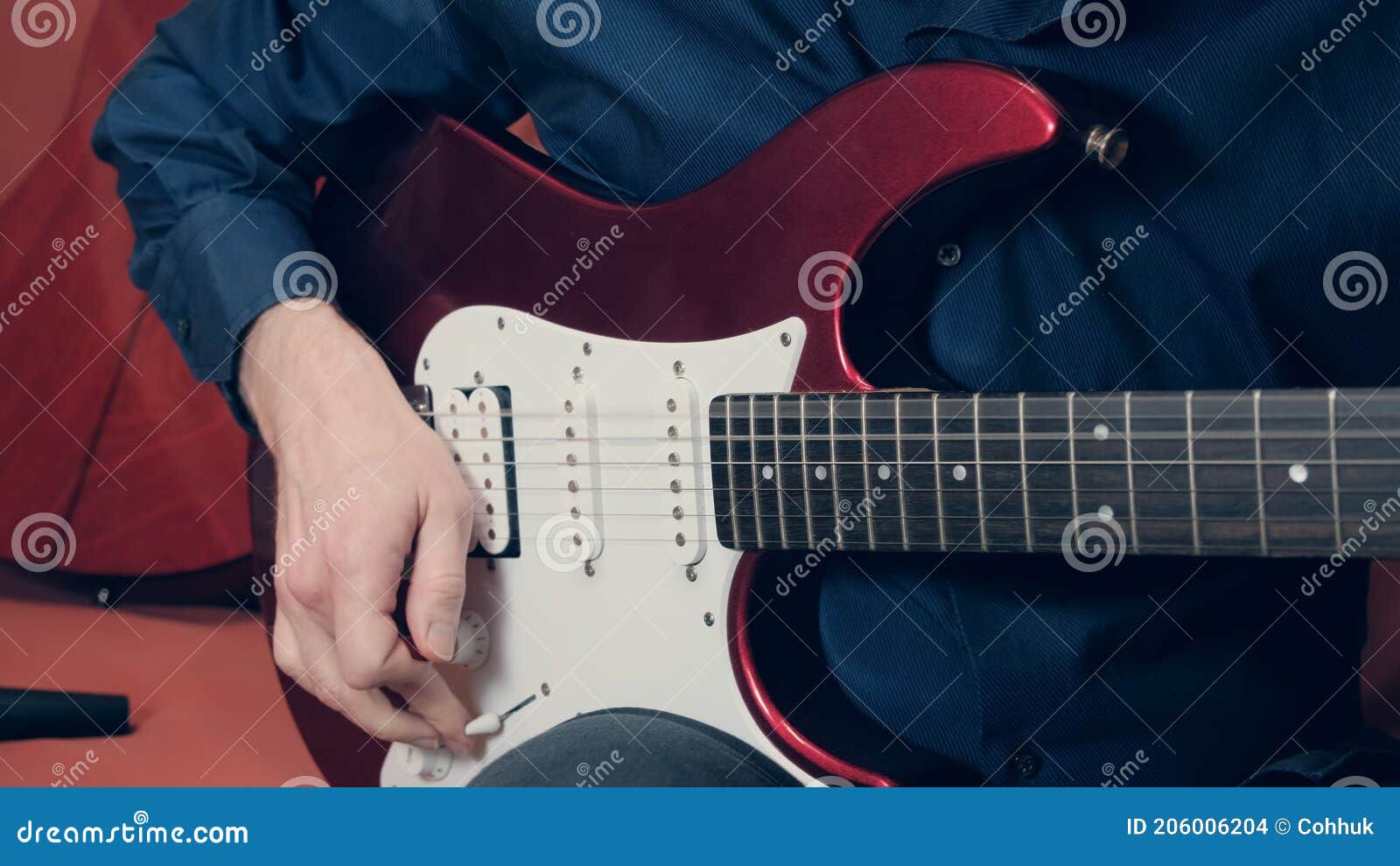 caucasian man in a blue shirt plays an red electric guitar