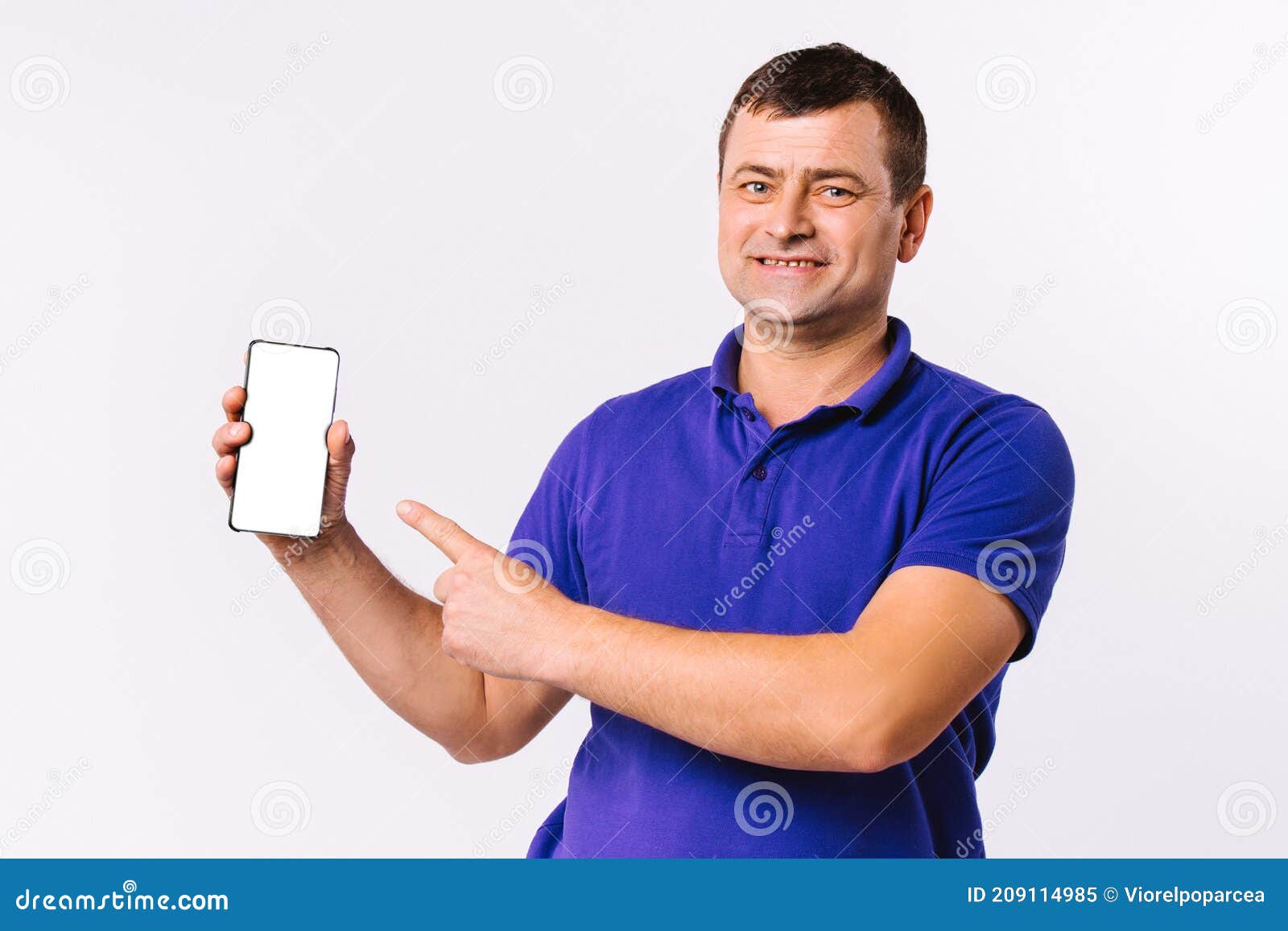 caucasian man in blue t-shirt looks happy at the camera and shows his forefinger at the mocks up smartphone screen. gray