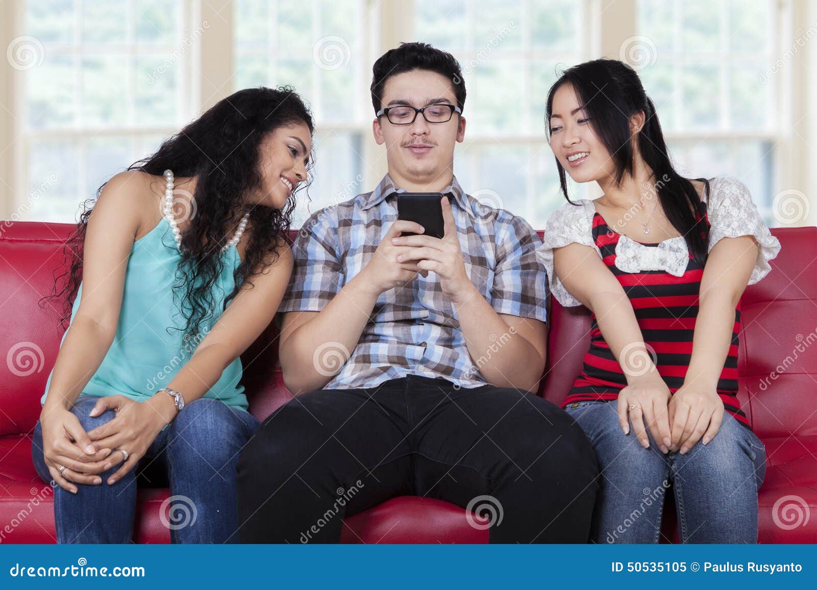 Caucasian man with curious girls. Portrait of caucasian person sitting on sofa with curios girls looking at his smartphone