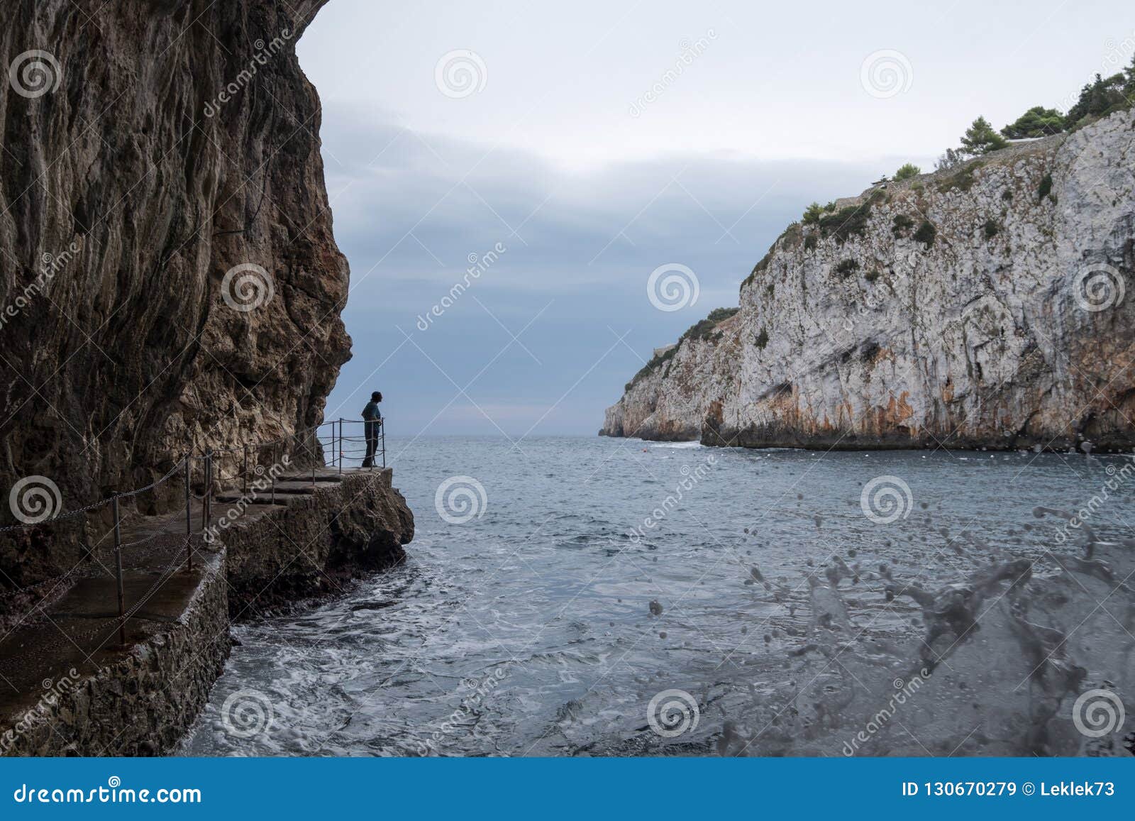 Zinzulusa Caves, near Castro on the Salento Peninsula in Puglia, Italy. Person stands on gang plank at entrance to the caves. Caves of Zinzulusa, near Castro on the Salento Peninsula in Puglia, Southern Italy. Person stands on gang plank at entrance to the caves.