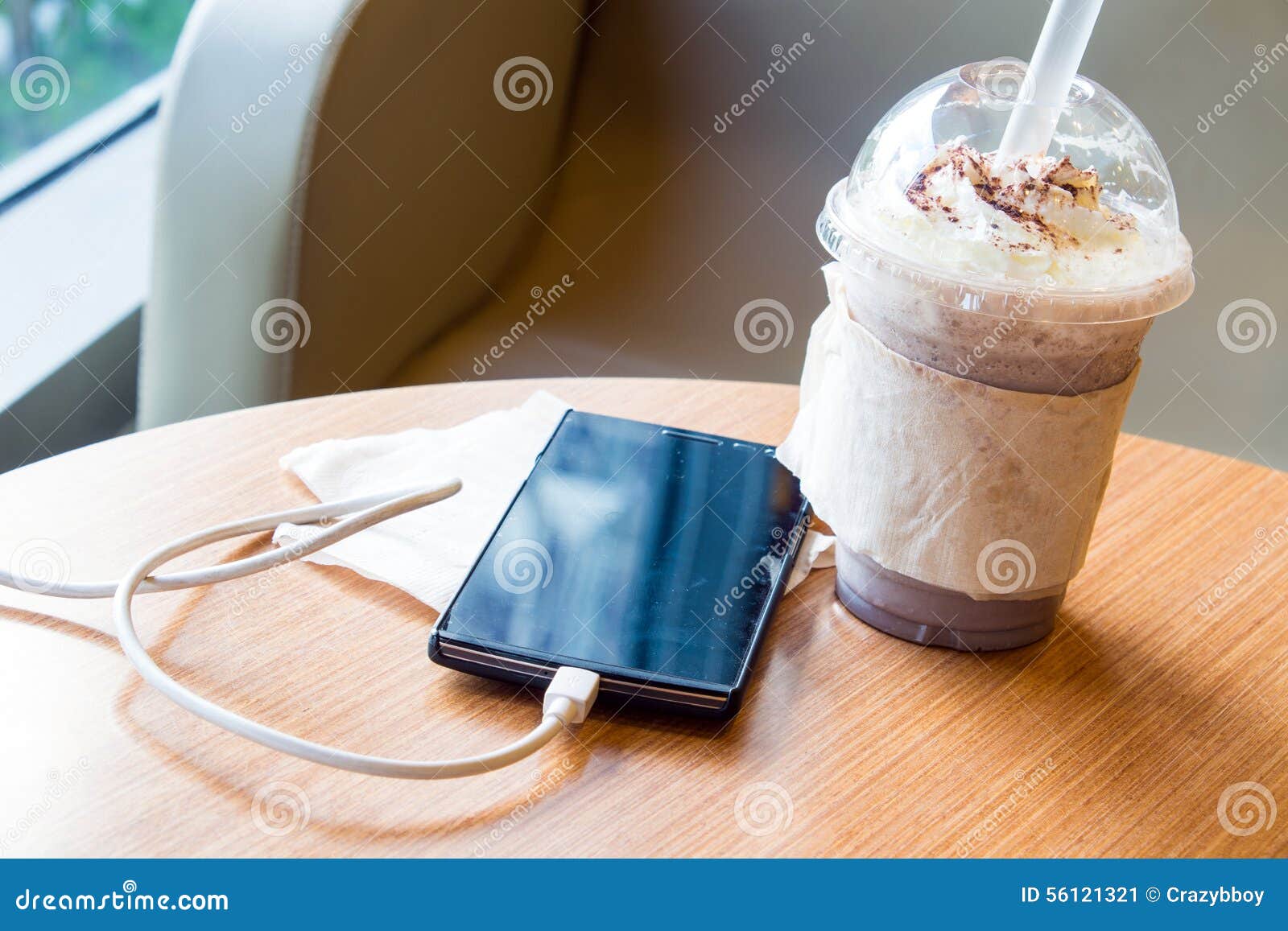cell phone charging in the cafe with a plastic cup of iced chocolate frappe