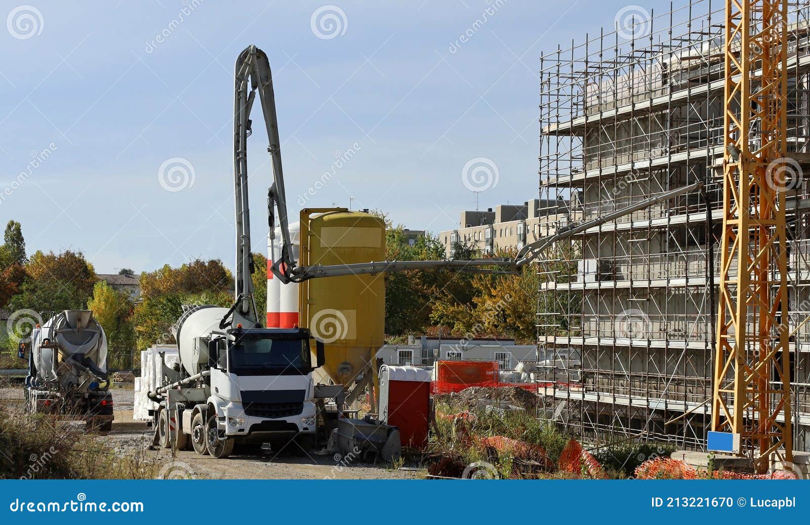 Cement Mixer Trucks at Work on a Facade Under Construction Covered with Scaffoldings Stock Photo