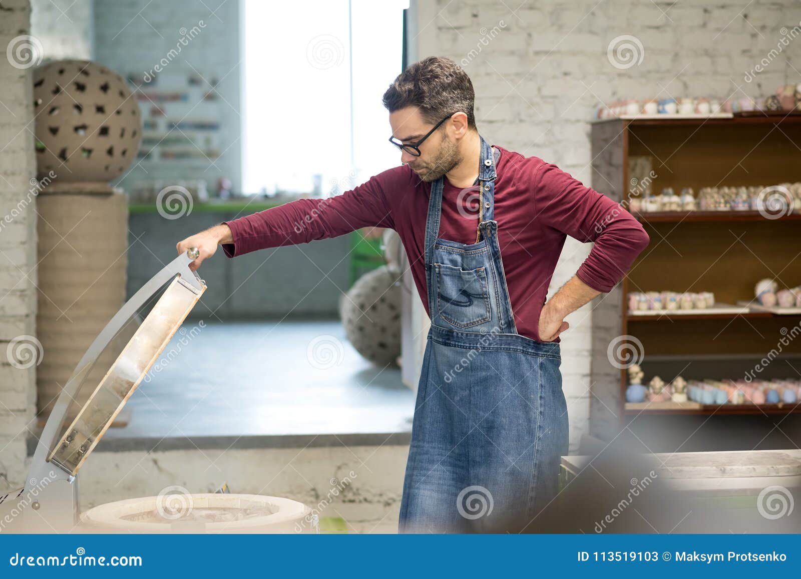 ceramist dressed in an apron setting the electric oven for drying the clay sculpture using control console.