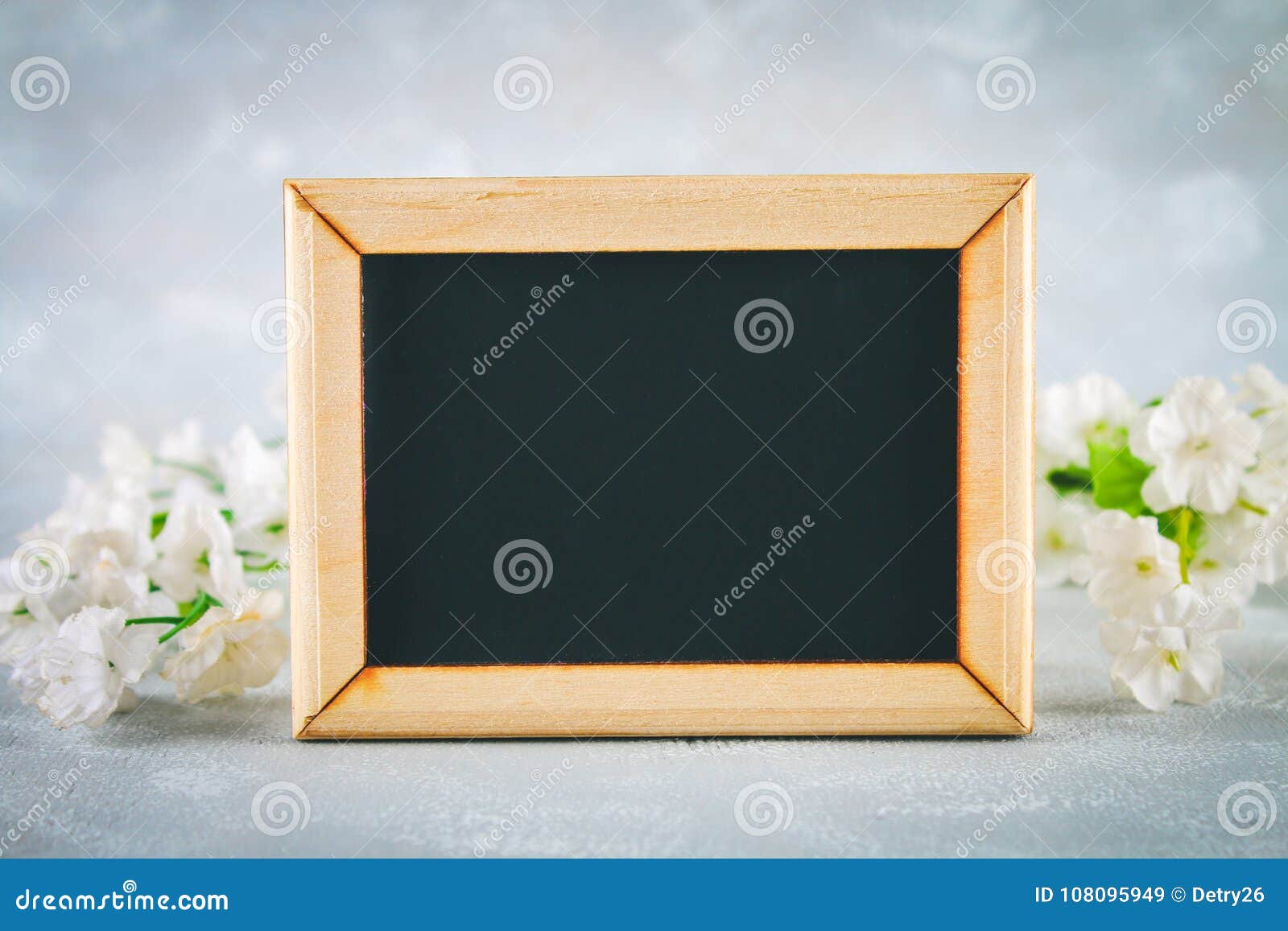 Chalkboard in a Wooden Frame with an Empty Box Surrounded by White Flowers on a Gray Background
