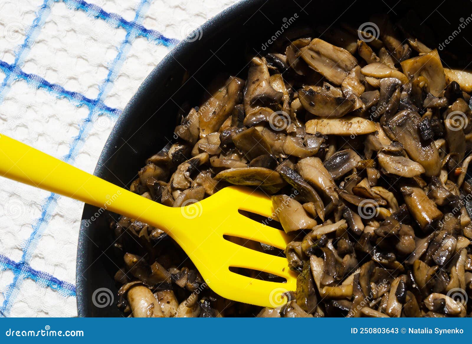 champignon mushrooms fried, cooked in a frying pan with a yellow spatula, close-up