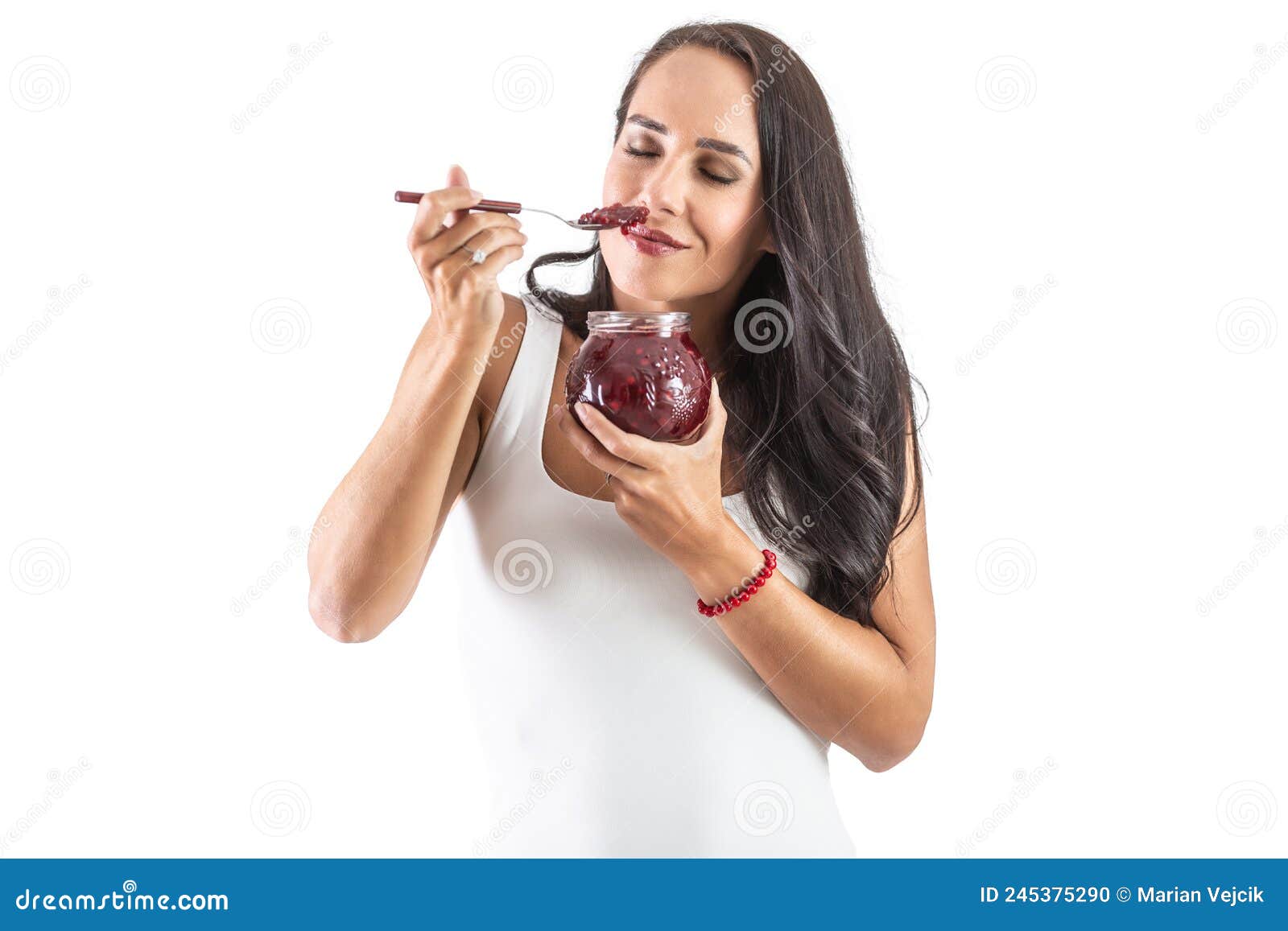 charming brunette is holding a spoon sull of jam and smelling the tasty and sweet aroma.  background