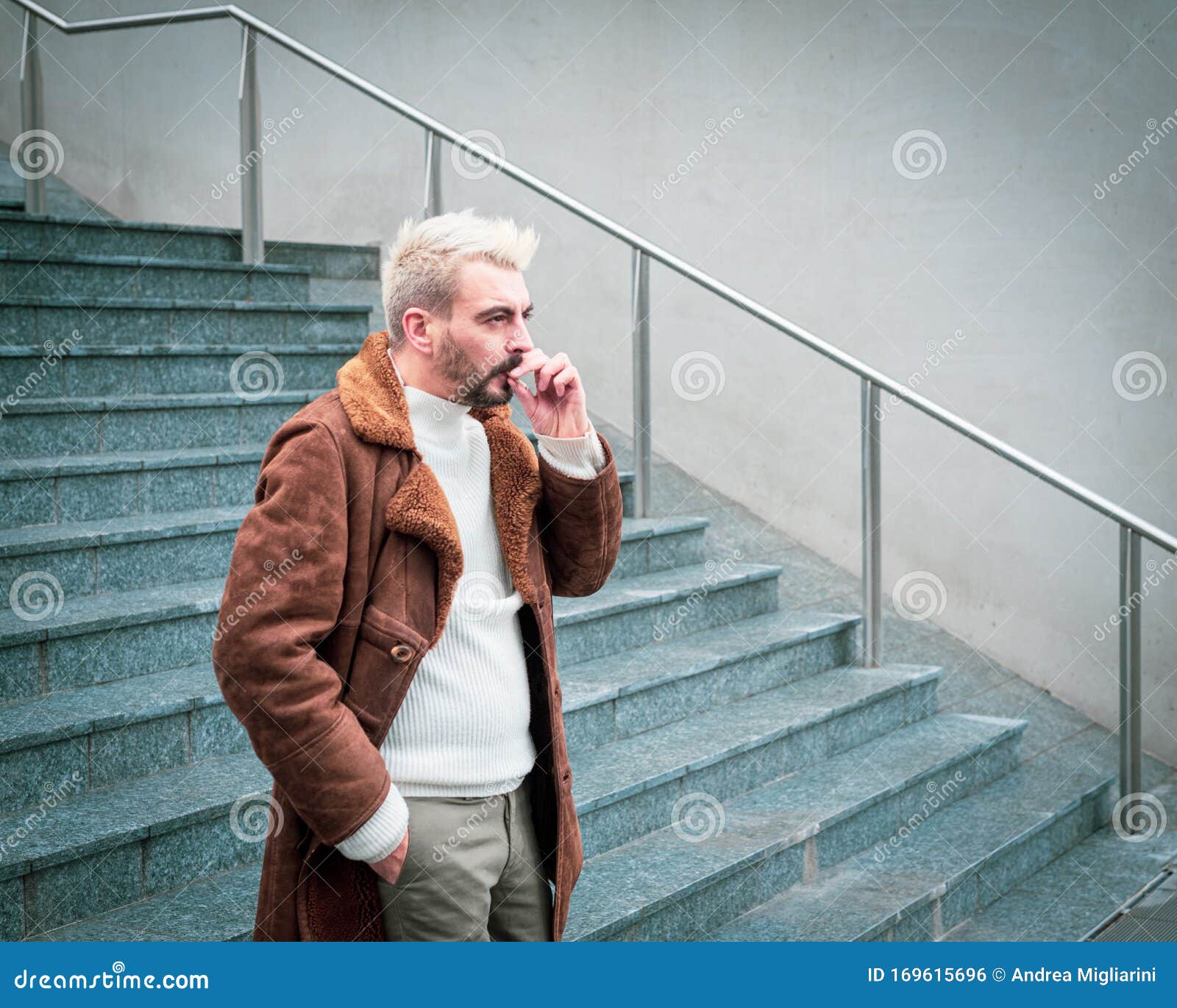 A Charming Hipster with Platinum Blonde Hair and Dark Beard Smokes a  Cigarette, Wears a White Sweater and a Brown Coat, Teal and Stock Photo -  Image of desaturated, cityscape: 169615696