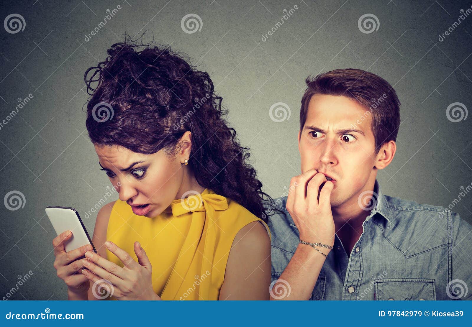 cheating boyfriend. man nervously biting fingernails while shocked girlfriend reading text messages on his mobile phone