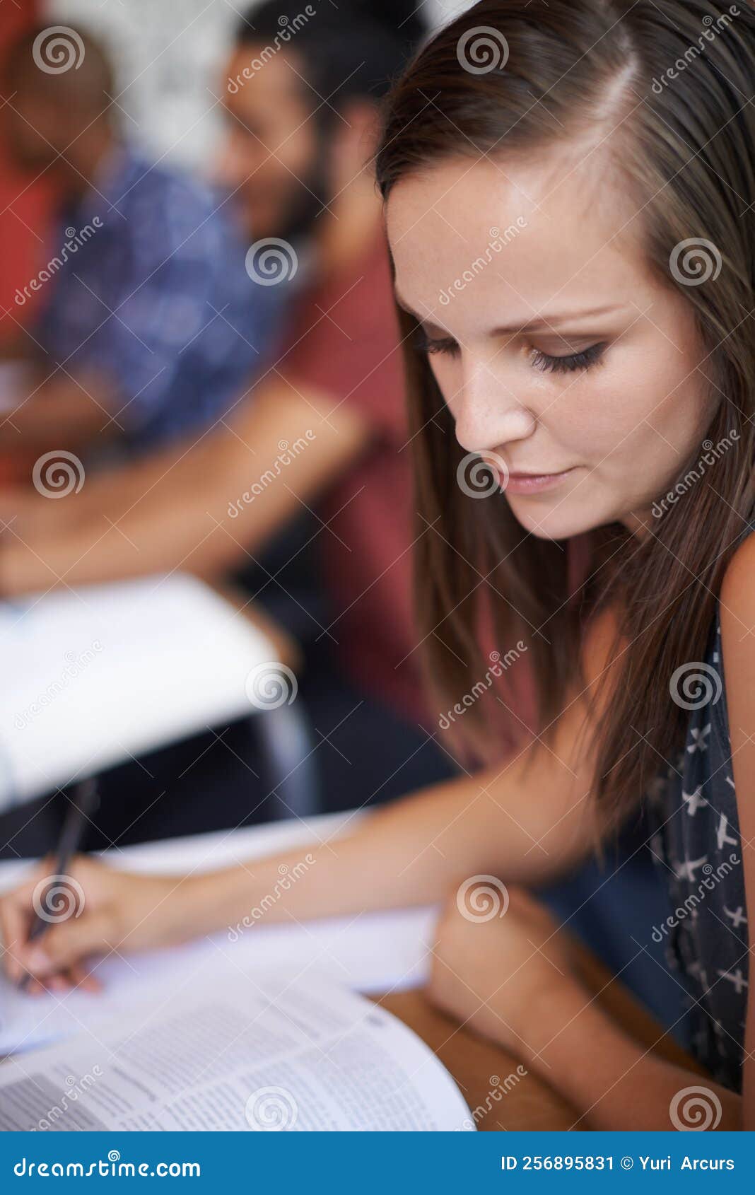 checking her resouces. an attractive young varsity student sitting in a classroom with a textbook in front of her.