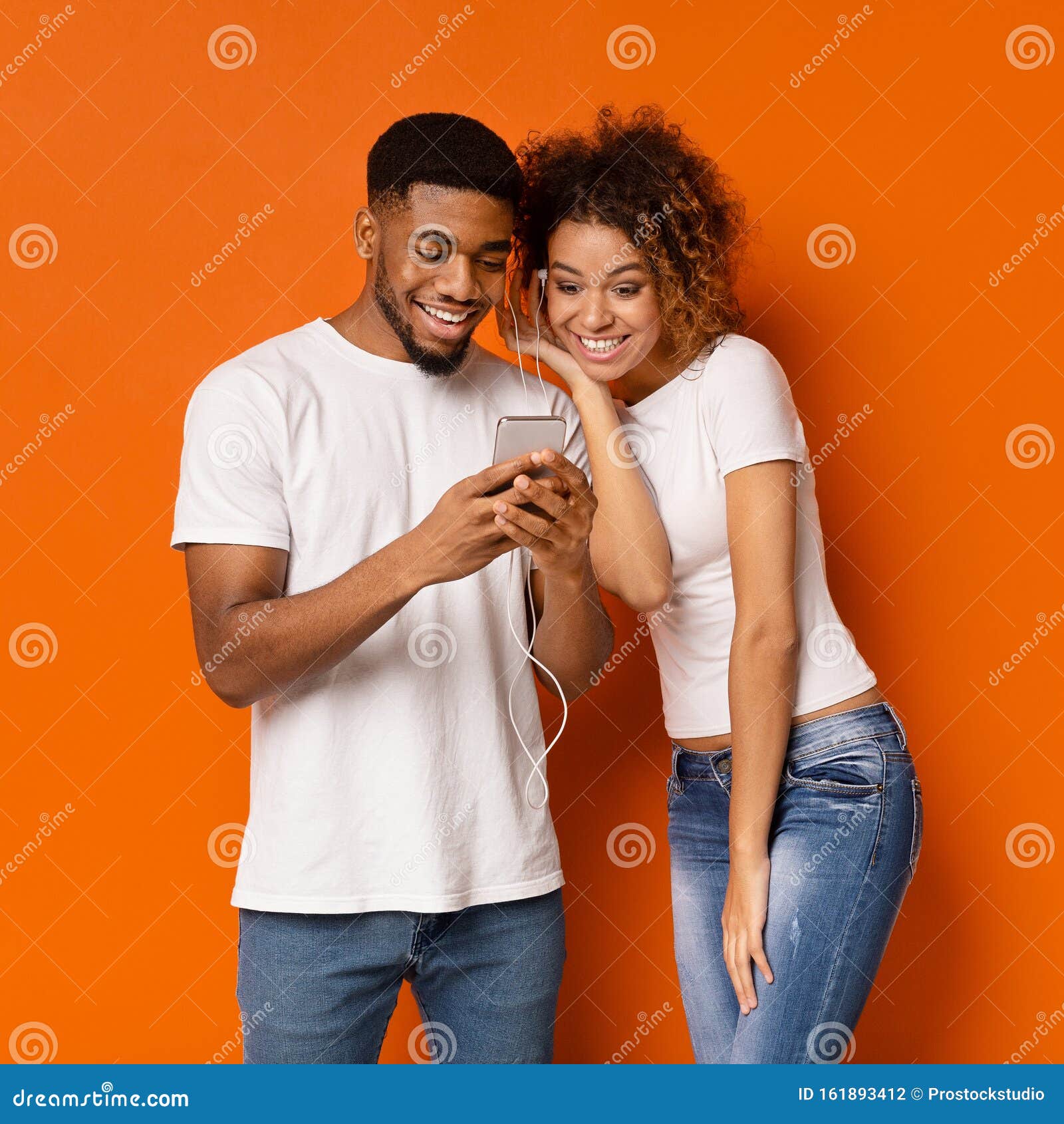 cheerful african man and woman listening to music on cellphone