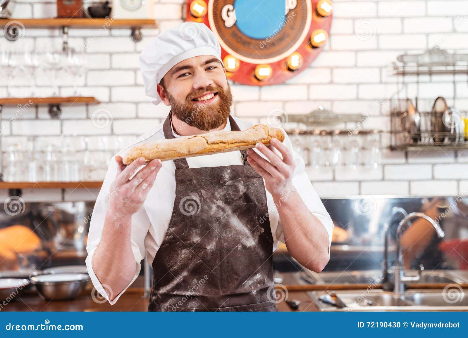 Cheerful young man baker standing at bakery holding bread Stock Photo by  vadymvdrobot