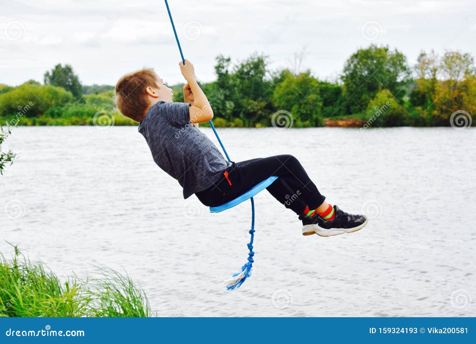Cheerful Boy Swinging on a Rope Swing Above the Water Stock Image