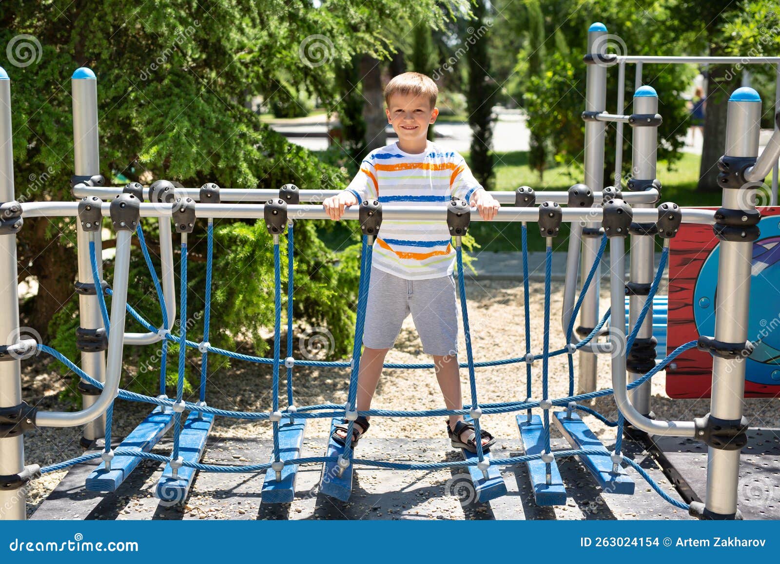 Cheerful Boy Walks on a Rope Bridge on a Playground in the Park. Stock