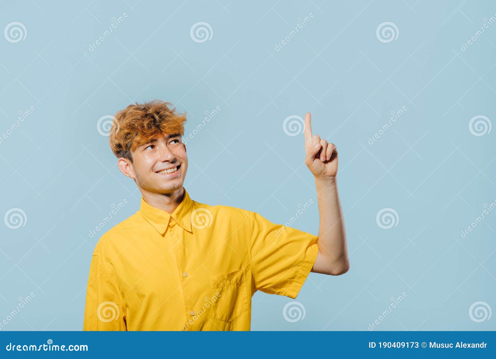 cheerful boy in yellow shirt pointing up direction on blue background,