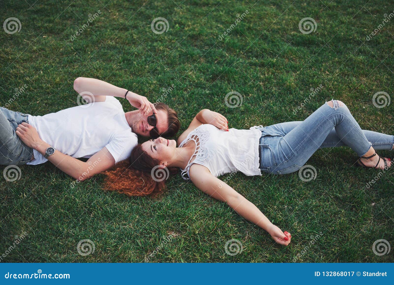 Cheerful Couple Lying On The Grass. Young People Outdoors. Happiness