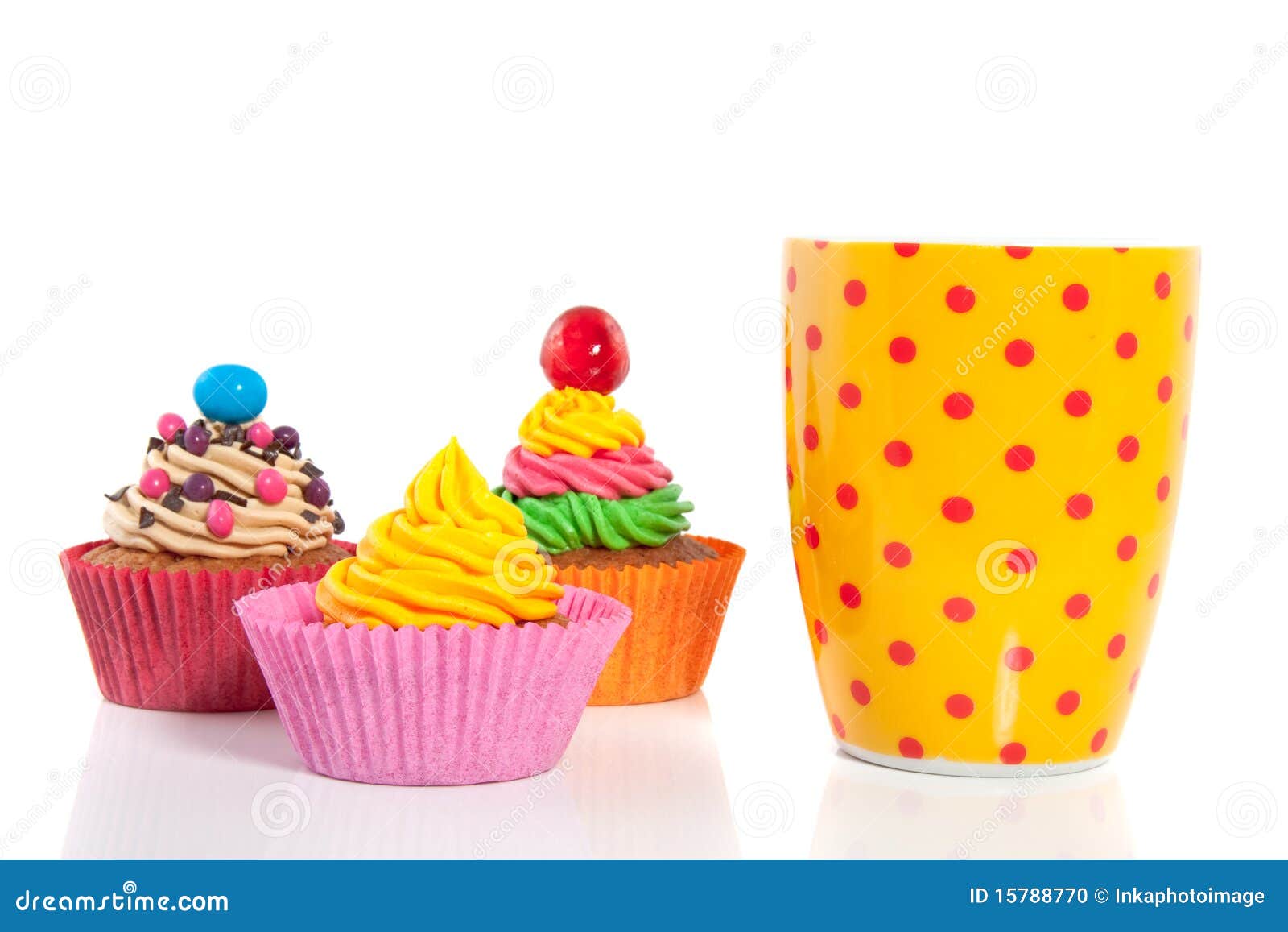 Cheerful cupcakes. Three colorful creamed cupcakes with a cherry and chocolate on top with a dotted tea cup isolated over white