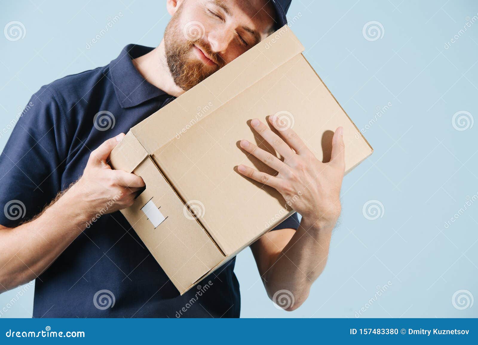 cheerful delivery man in uniform is hugging cardboard box with his eyes closed