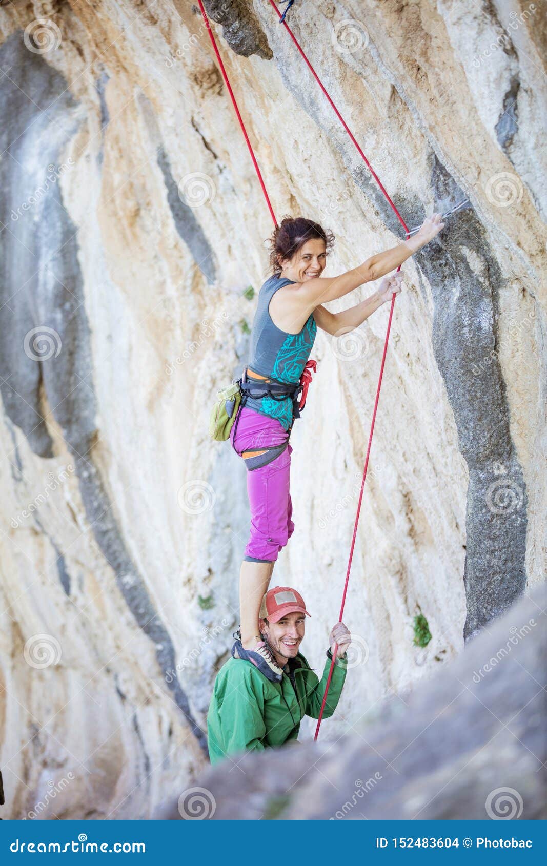 female rock climber standing on shoulders of her partner in order to start climbing challenging route