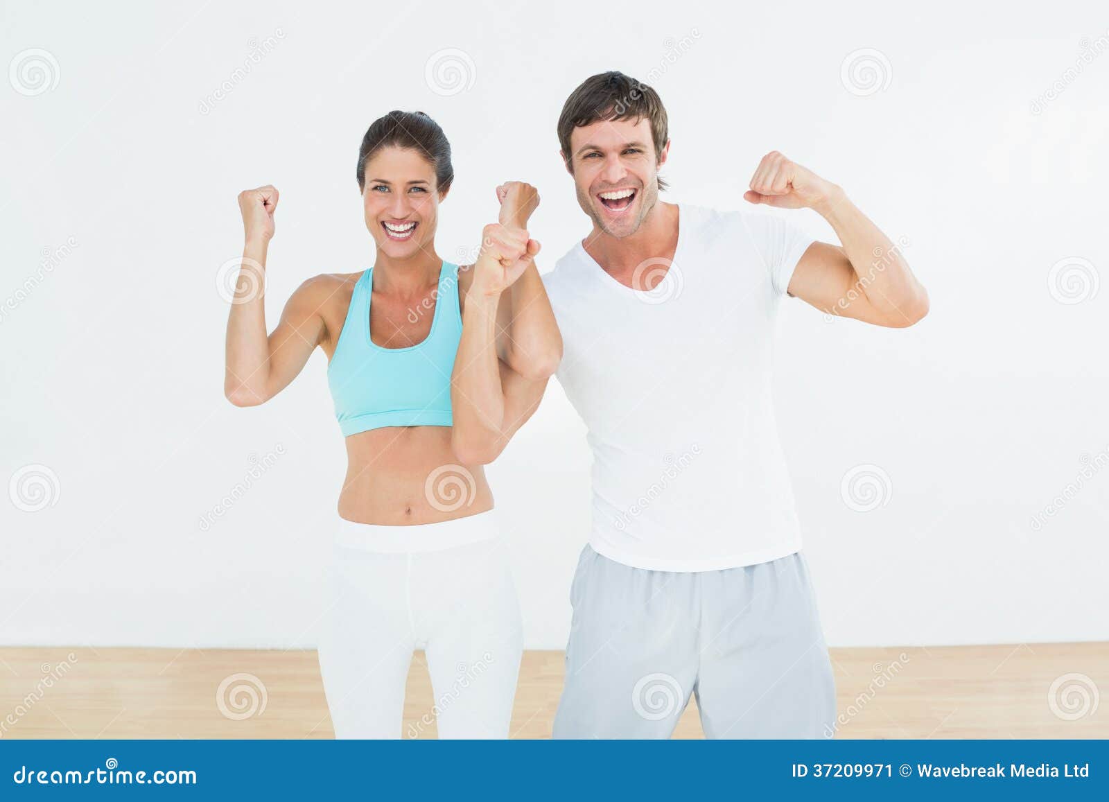 cheerful fit couple clenching fists in fitness studio
