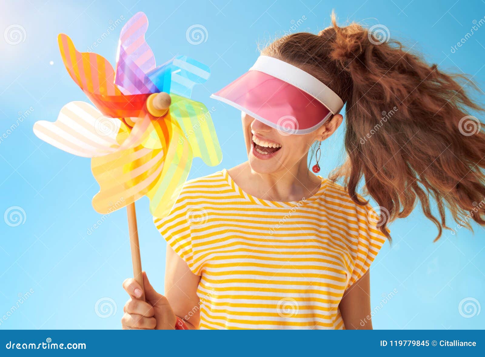 woman hiding behind sun visor holding colorful windmill