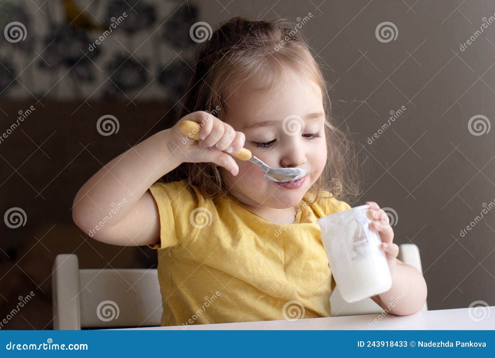 cheerful little girl eating plain homemade yogurt using spoon. healthy smiling kid, organic natural food