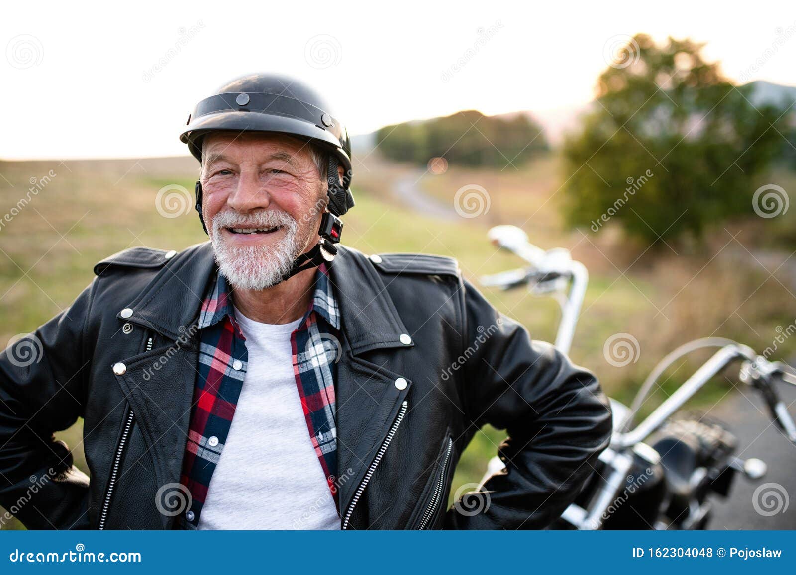 A Cheerful Senior Man Traveller with Motorbike in Countryside, Standing ...