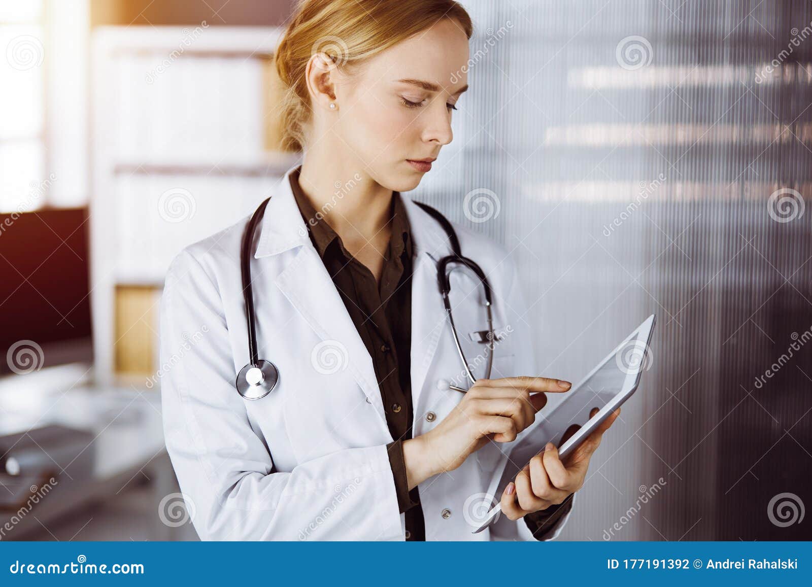 Cheerful Smiling Female Doctor Using Tablet Computer In Sunny Clinic